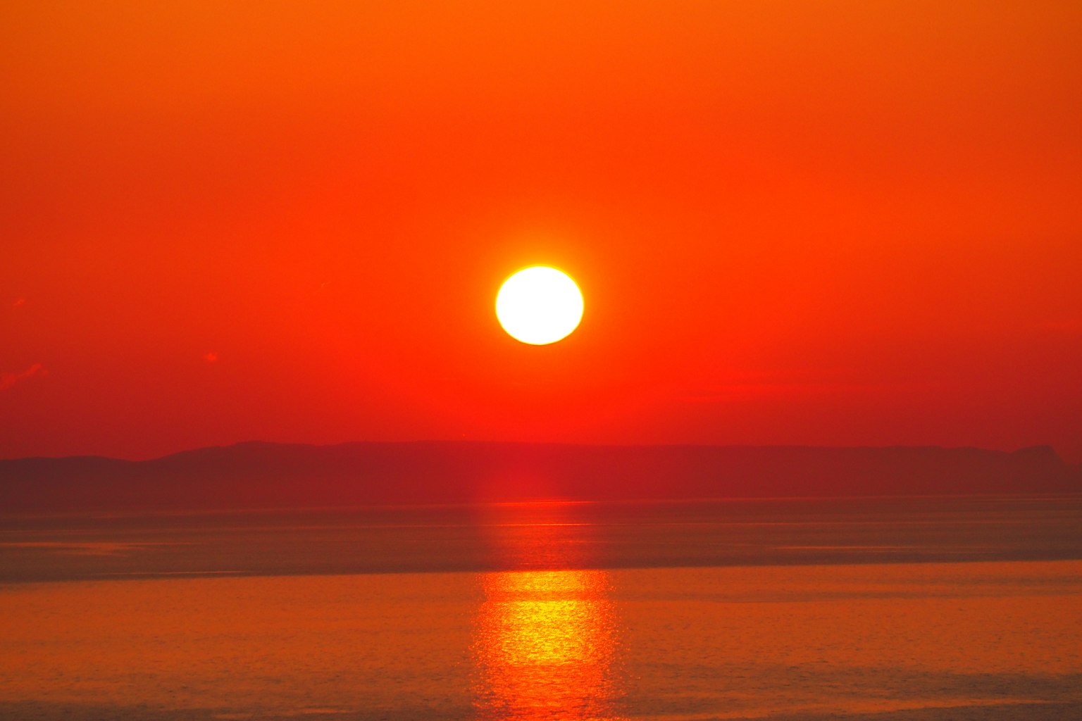 Schöner Sonnenuntergang mit lebhaft orangefarbenem Himmel und Sonne, die sich im Wasser spiegelt