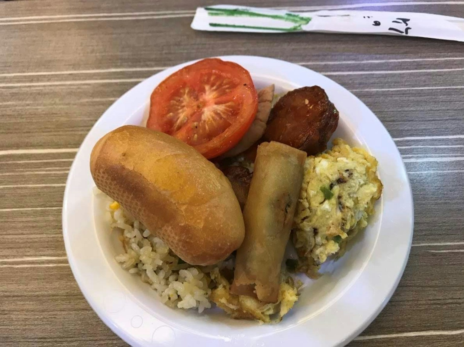 Un plato con arroz, rodajas de tomate, rollitos de primavera, albóndigas y un bollo