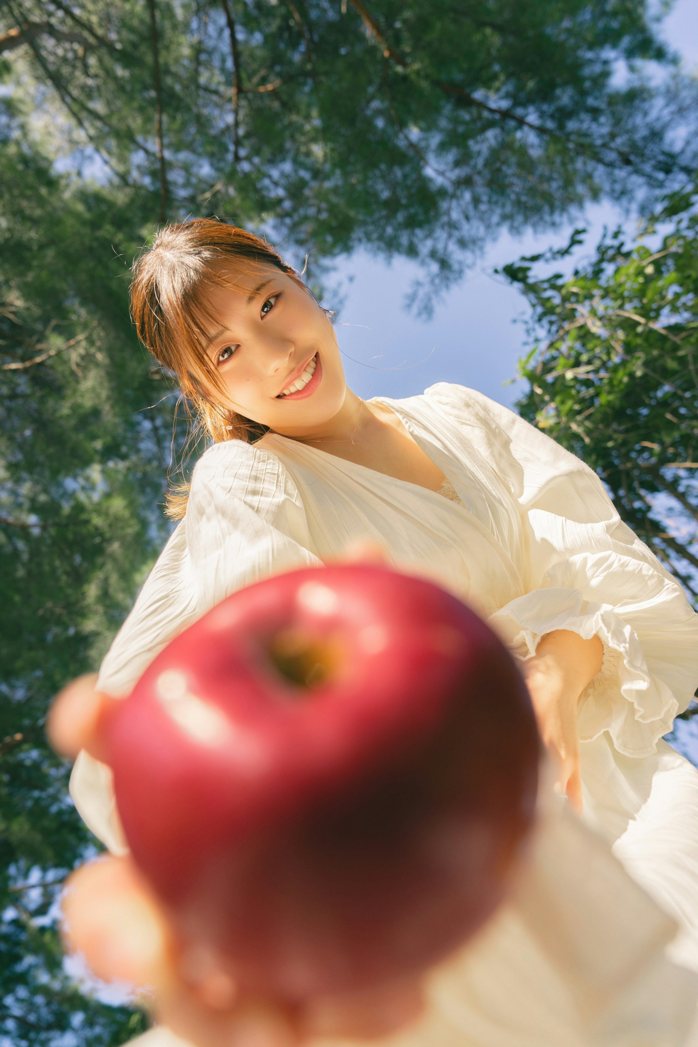 smiling woman offering an apple outdoors under blue sky