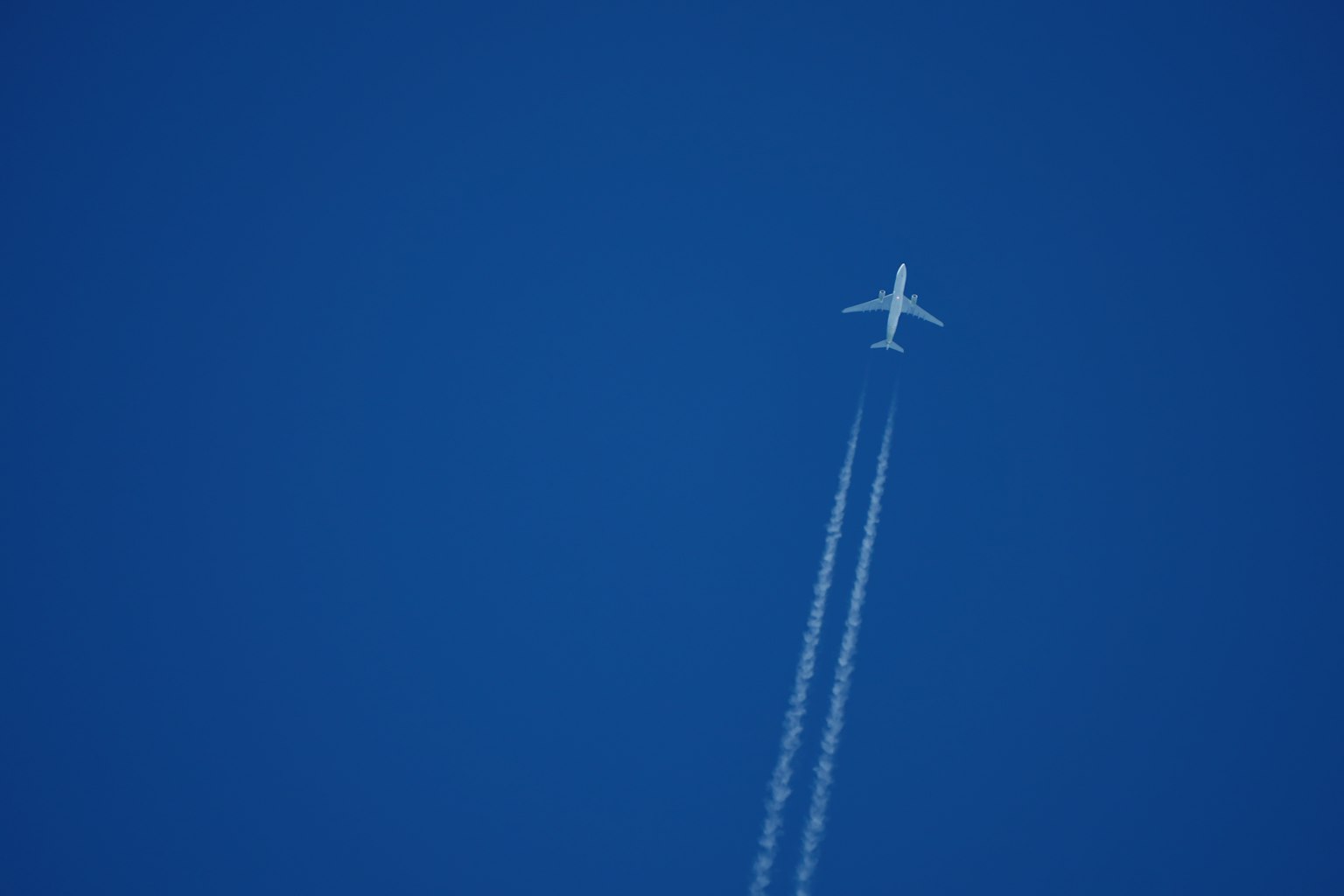 Ein Flugzeug fliegt in einem blauen Himmel mit Kondensstreifen dahinter
