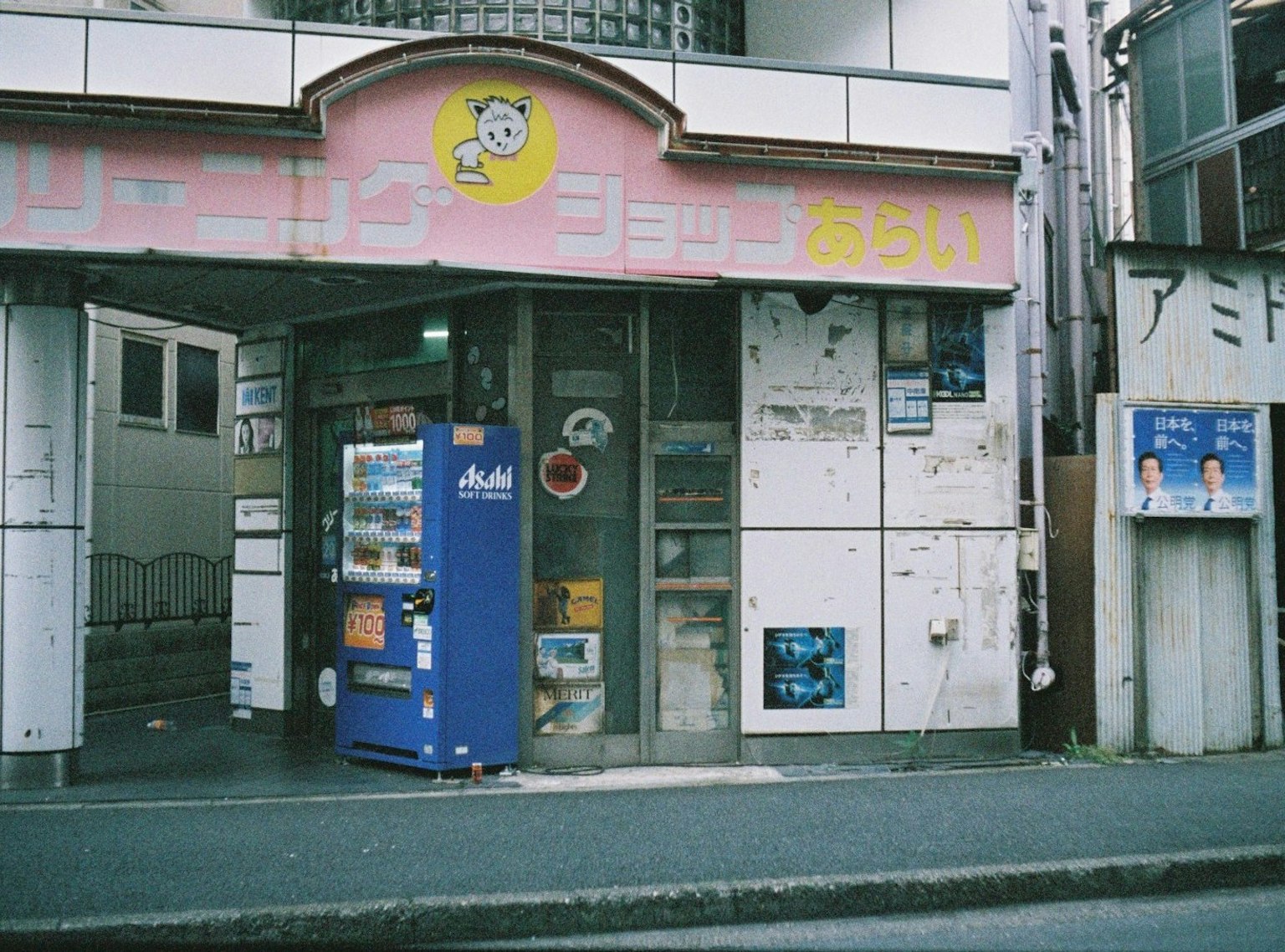 Un ingresso di un negozio con un'insegna rosa distintiva e un distributore automatico davanti