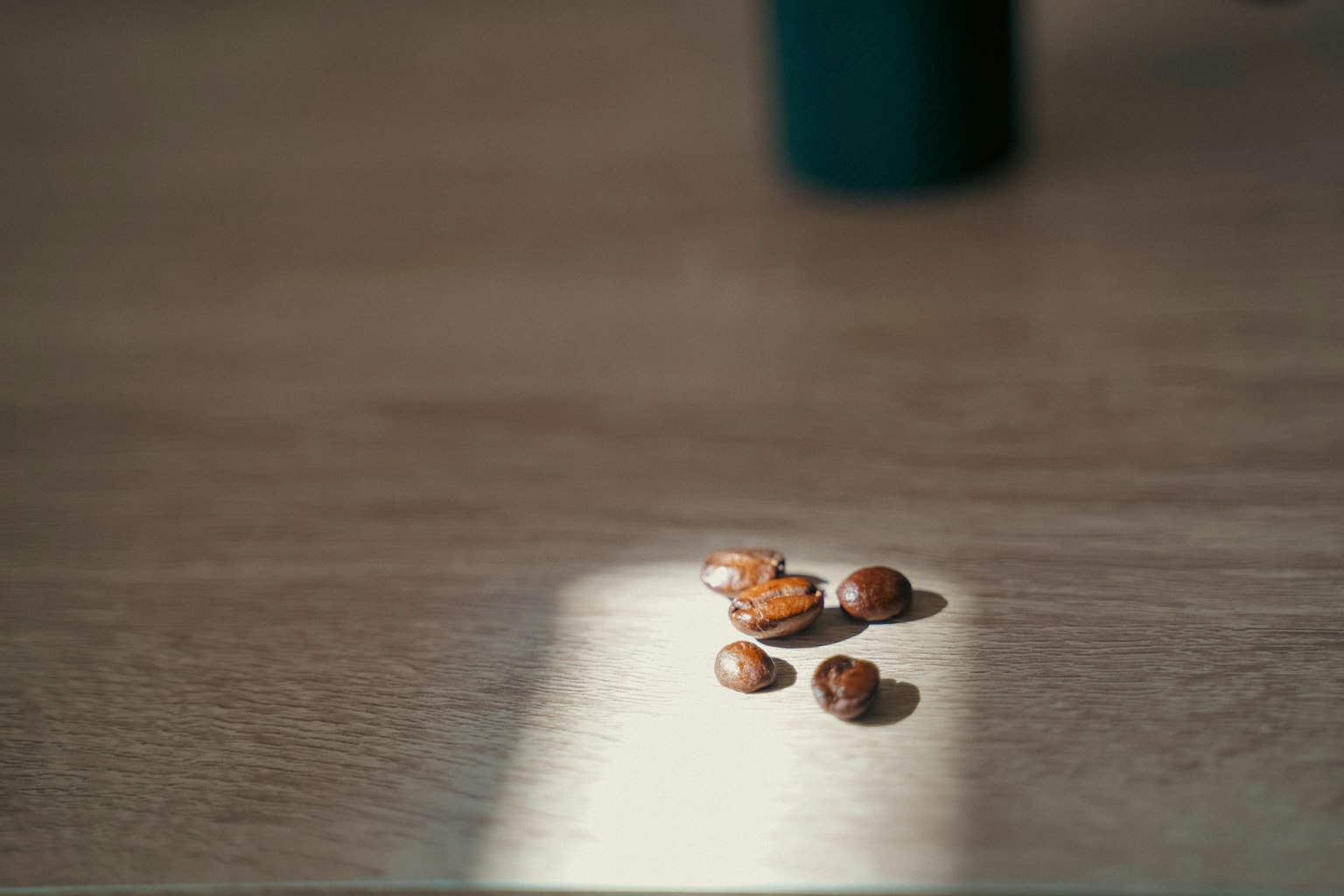 Granos de café sobre una mesa de madera con luz suave y sombra