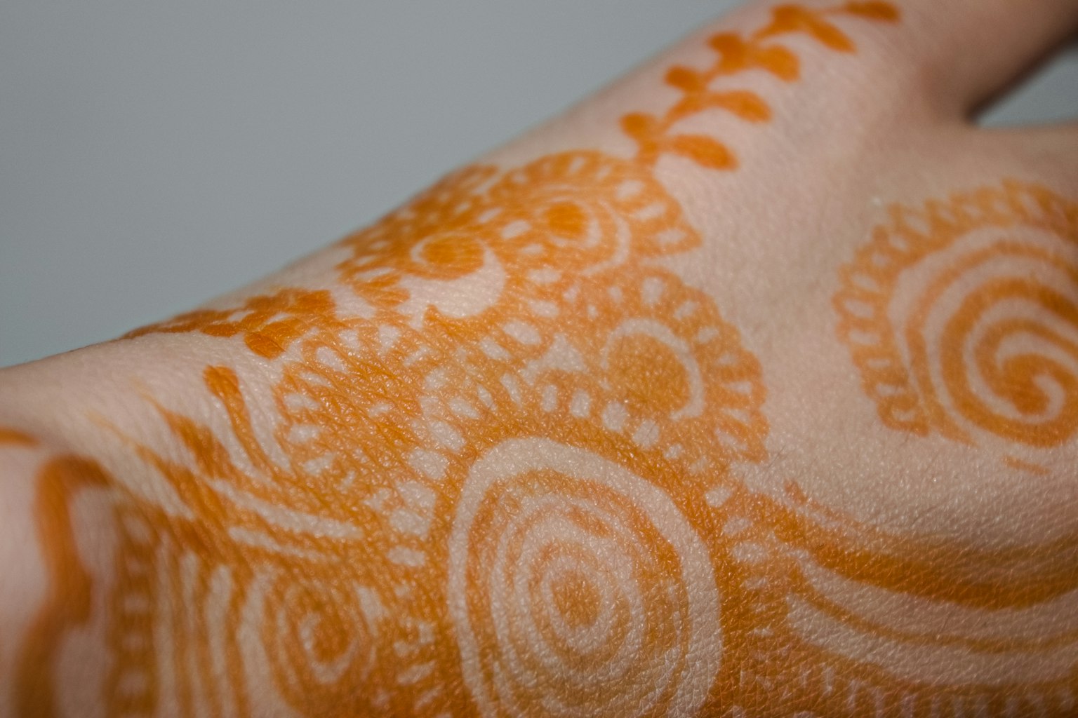 A hand adorned with orange henna tattoos featuring spiral patterns and floral designs