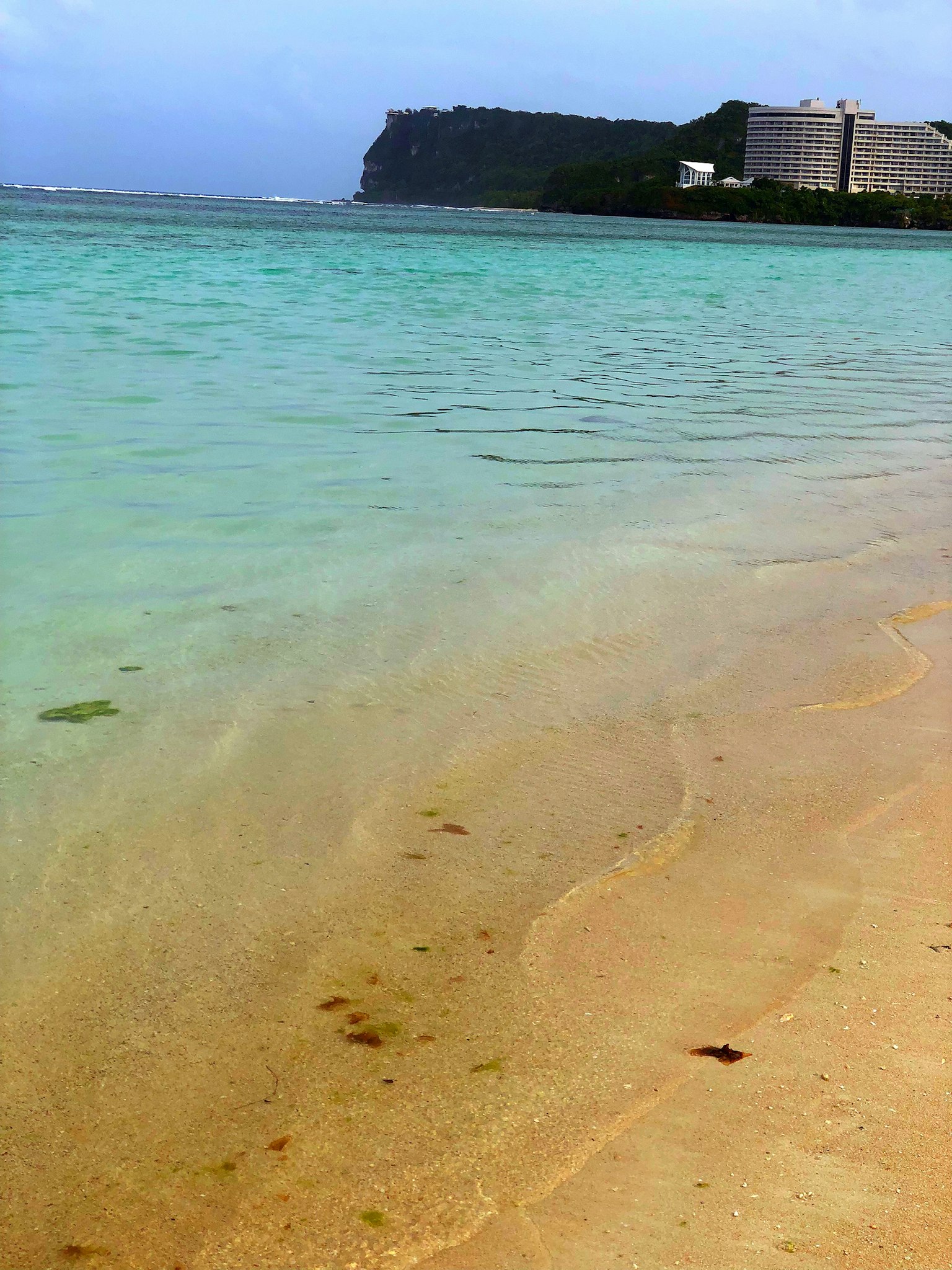 Scenic view of blue ocean and sandy beach with mountains in the distance