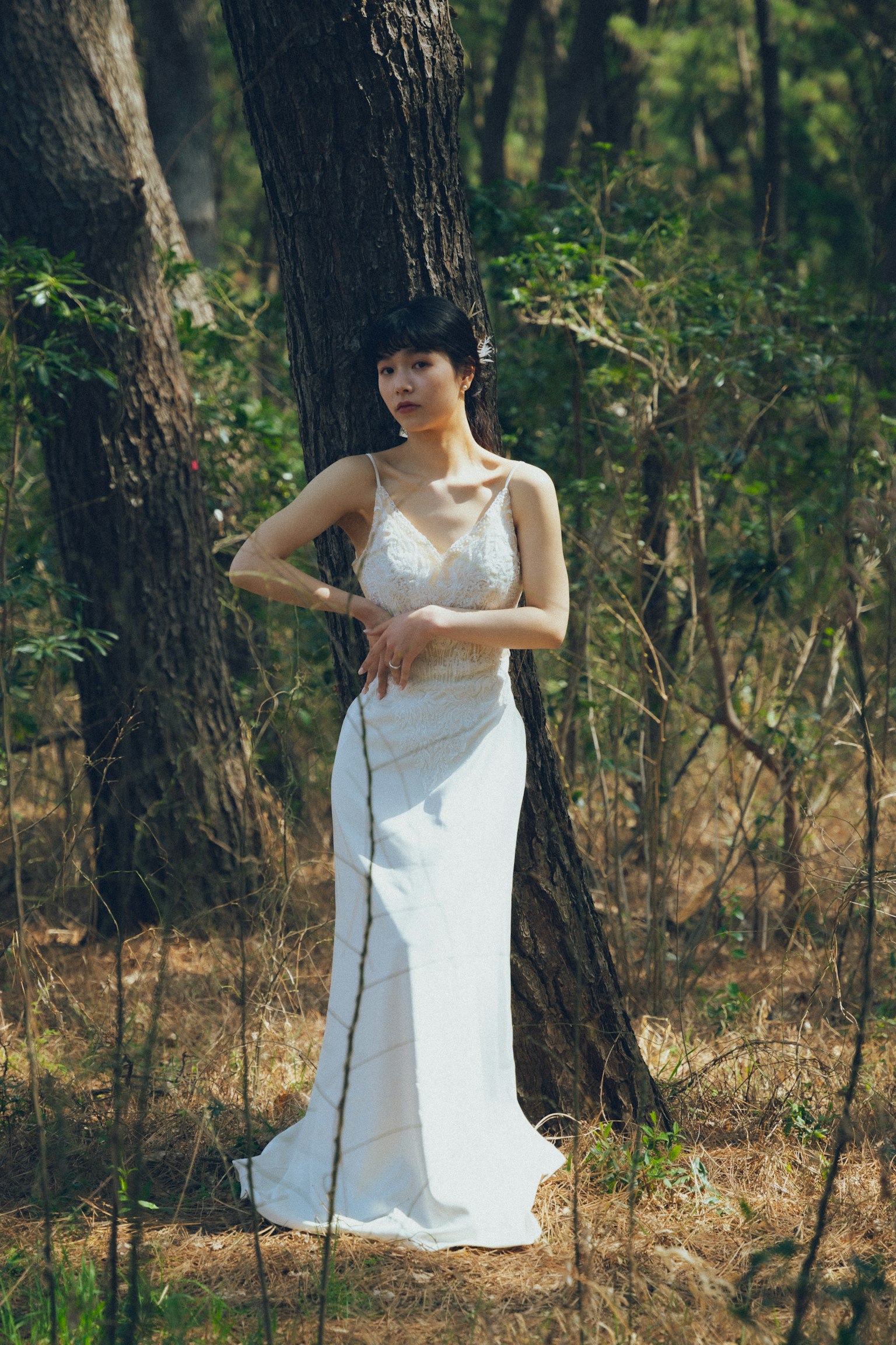 Una mujer con un vestido blanco de pie junto a un árbol en un entorno forestal