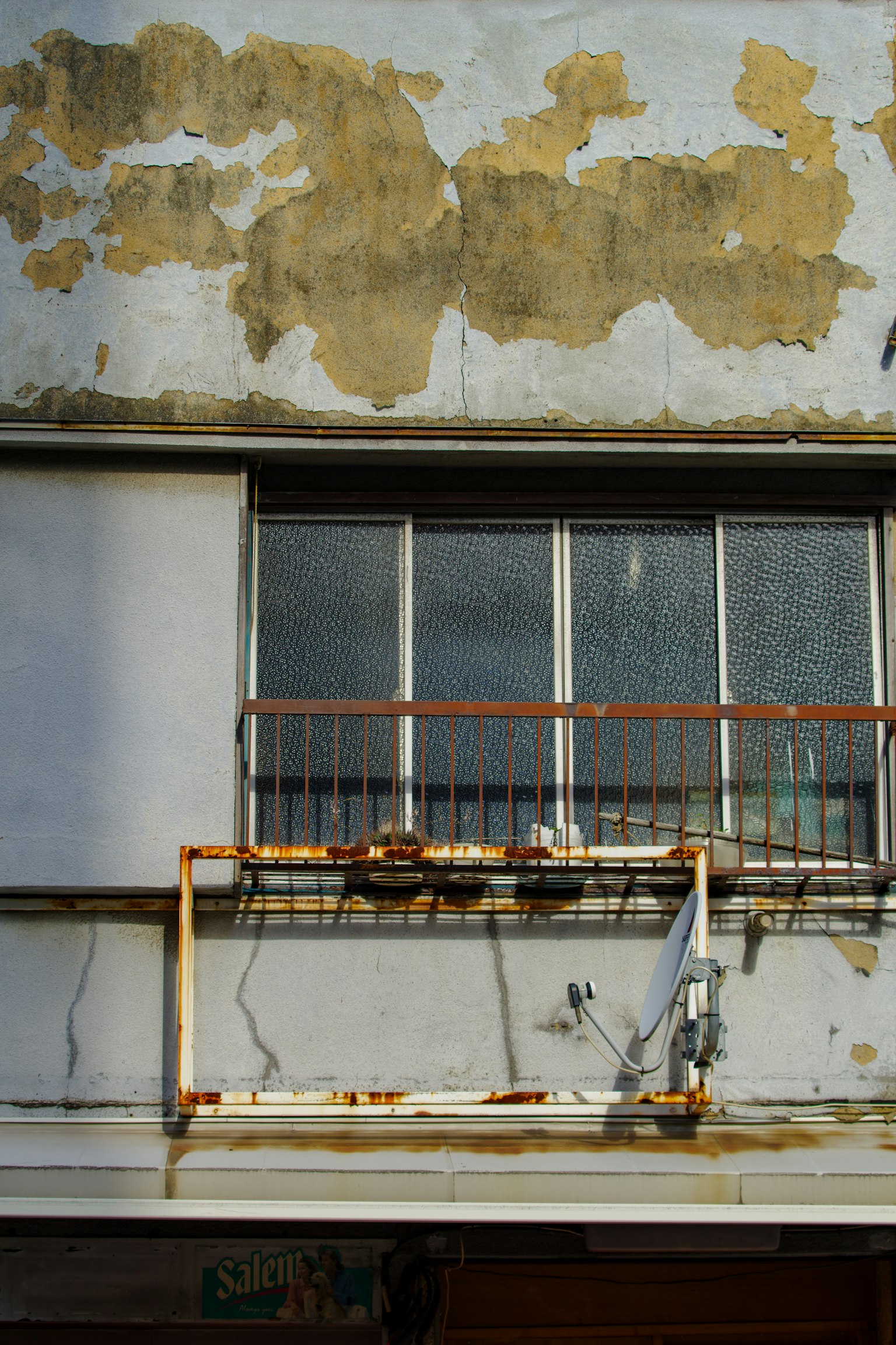 Weathered building facade with peeling paint and rusted balcony railing