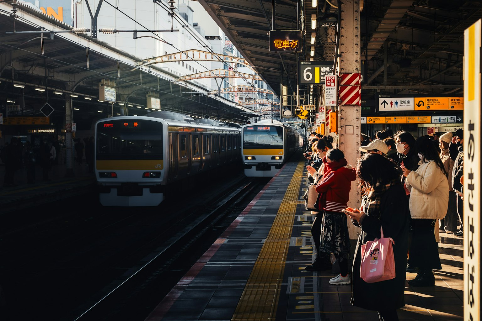 Menschen warten auf einem Bahnsteig mit ankommenden Zügen
