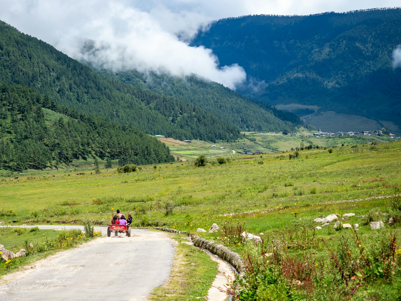 绿色山脉和多云蓝天的风景，两人沿着道路行走