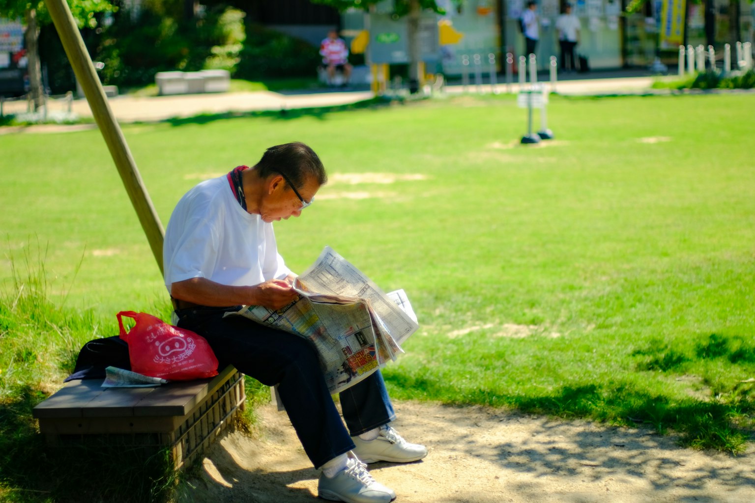 Un uomo anziano seduto su una panchina del parco che legge un giornale