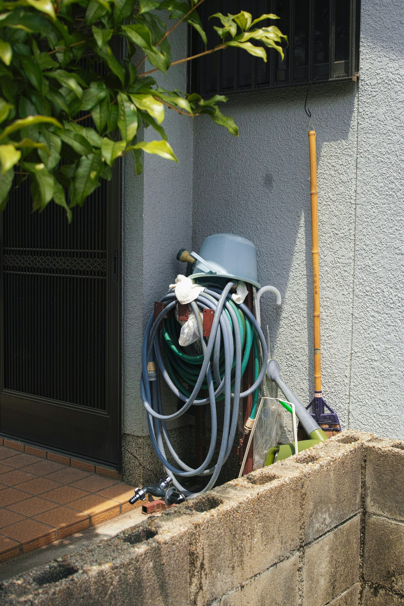 Un tuyau de jardin enroulé à côté d'un seau et d'un balai contre un mur