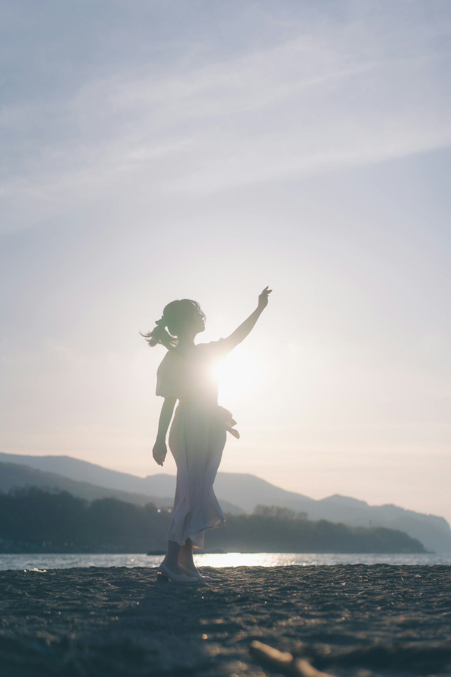 夕日を背にした女性のシルエットが海岸に立っている