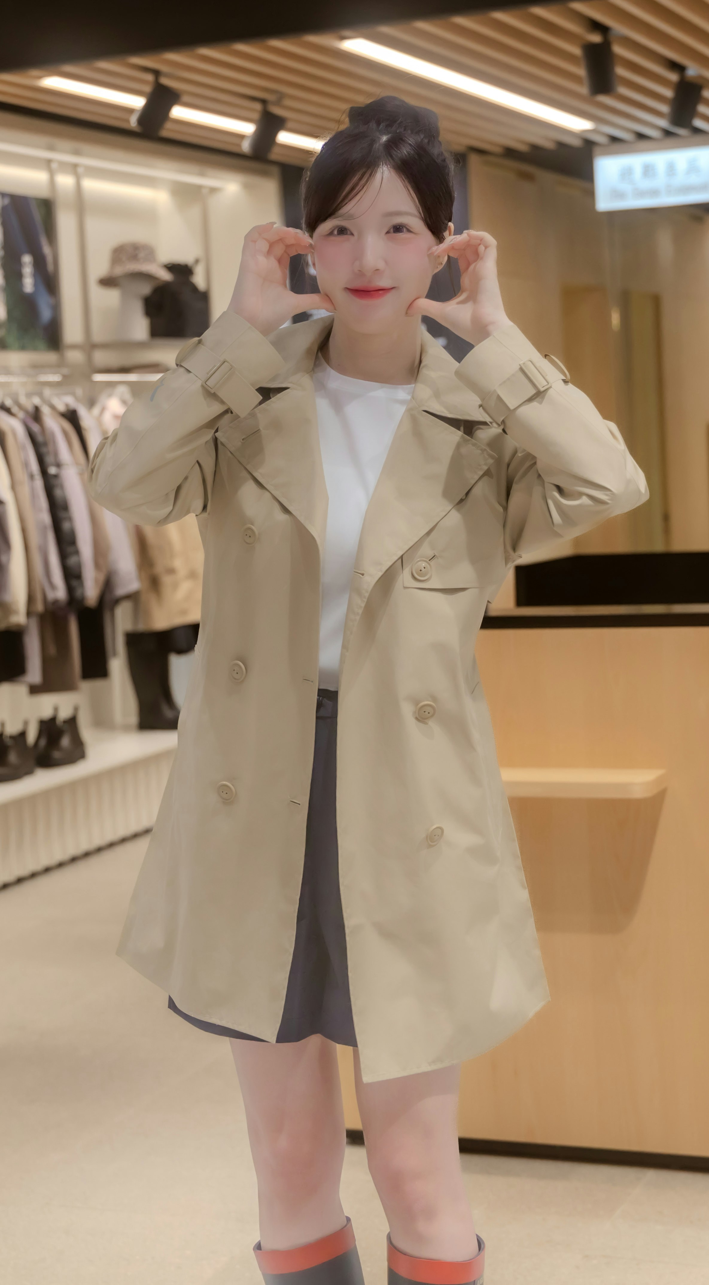 試着室の鏡前でポーズをとるベージュのトレンチコートの女性