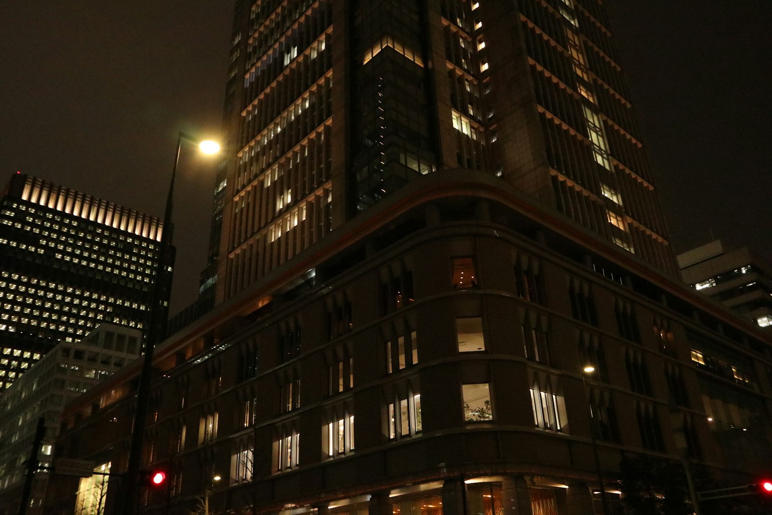 Nächtliche Stadtansicht mit einem hohen Gebäude, das von Straßenlaternen und hellen Fenstern beleuchtet wird