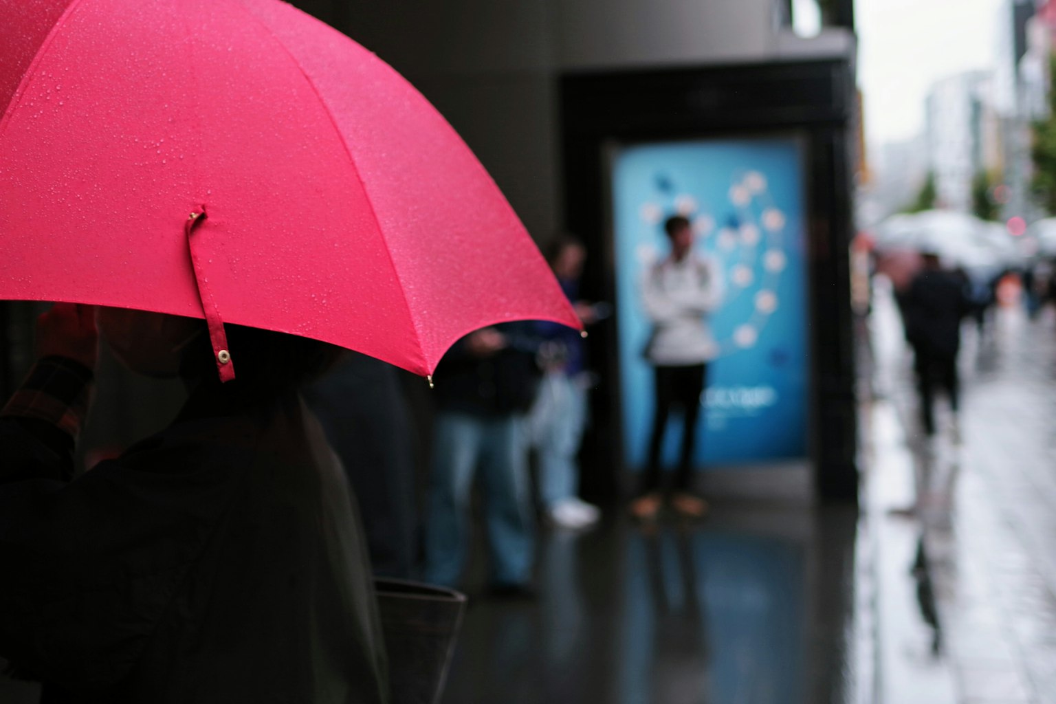 Persona sosteniendo un paraguas rosa bajo la lluvia con un anuncio azul de fondo