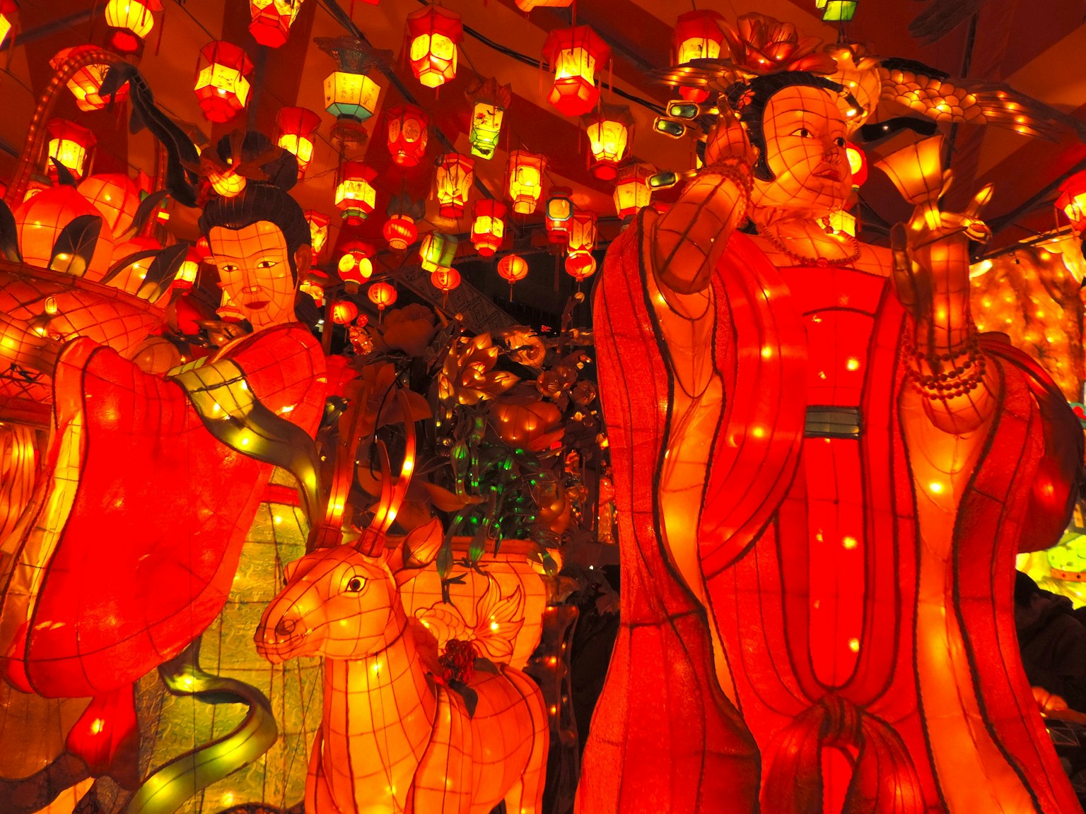รูปปั้นในชุดสีแดงล้อมรอบด้วยโคมไฟหลากสีและแสงสว่าง