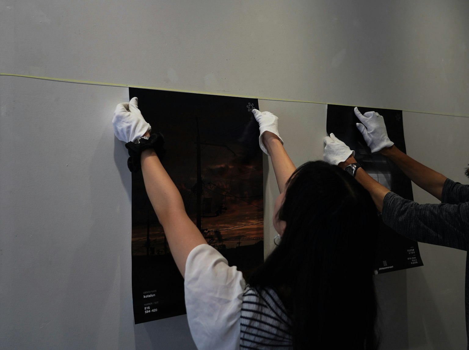 People hanging posters at an exhibition with gloved hands