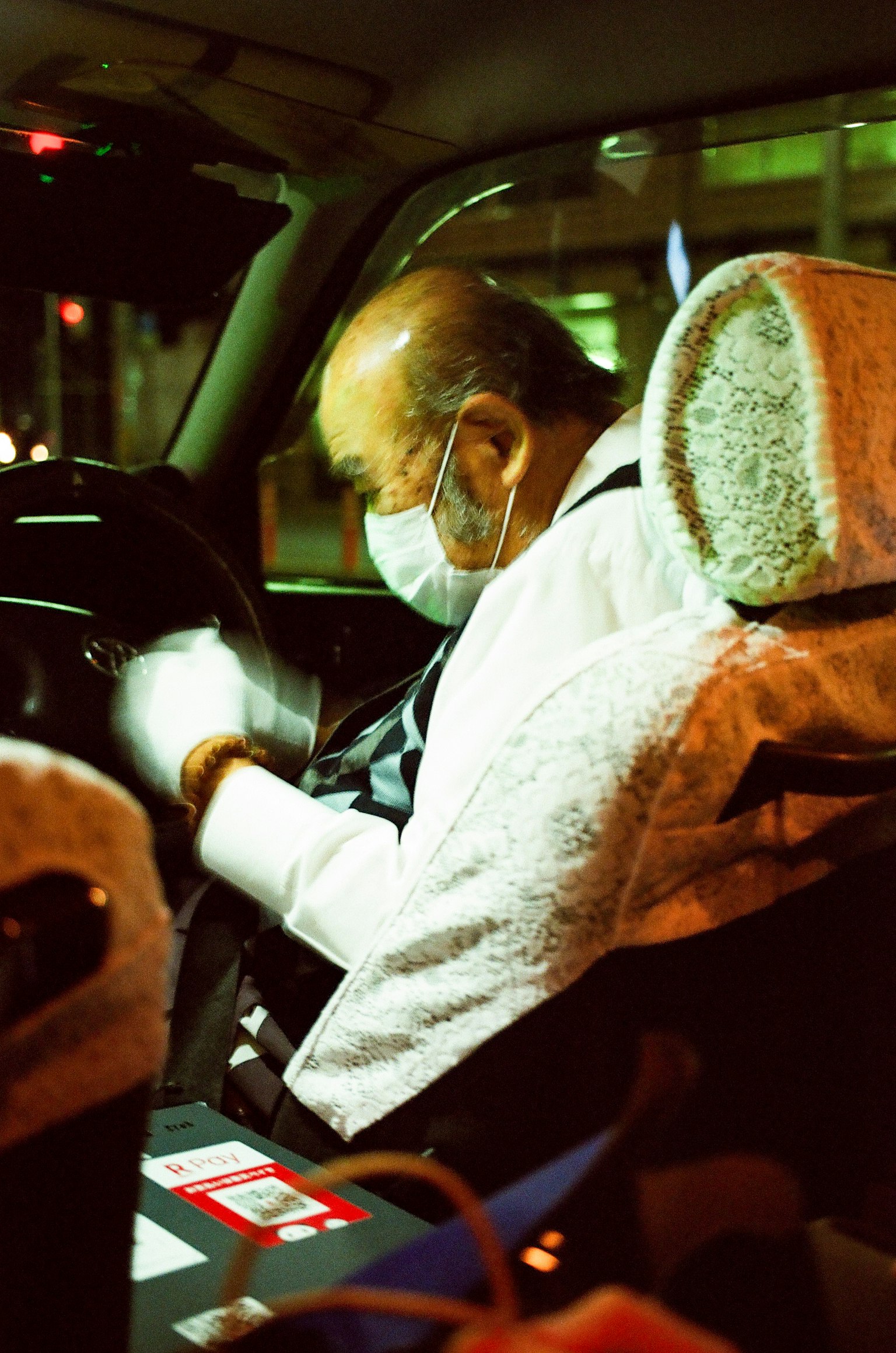 Ein männlicher Fahrer mit Maske, der das Lenkrad nachts mit Stadtlichtern im Hintergrund hält