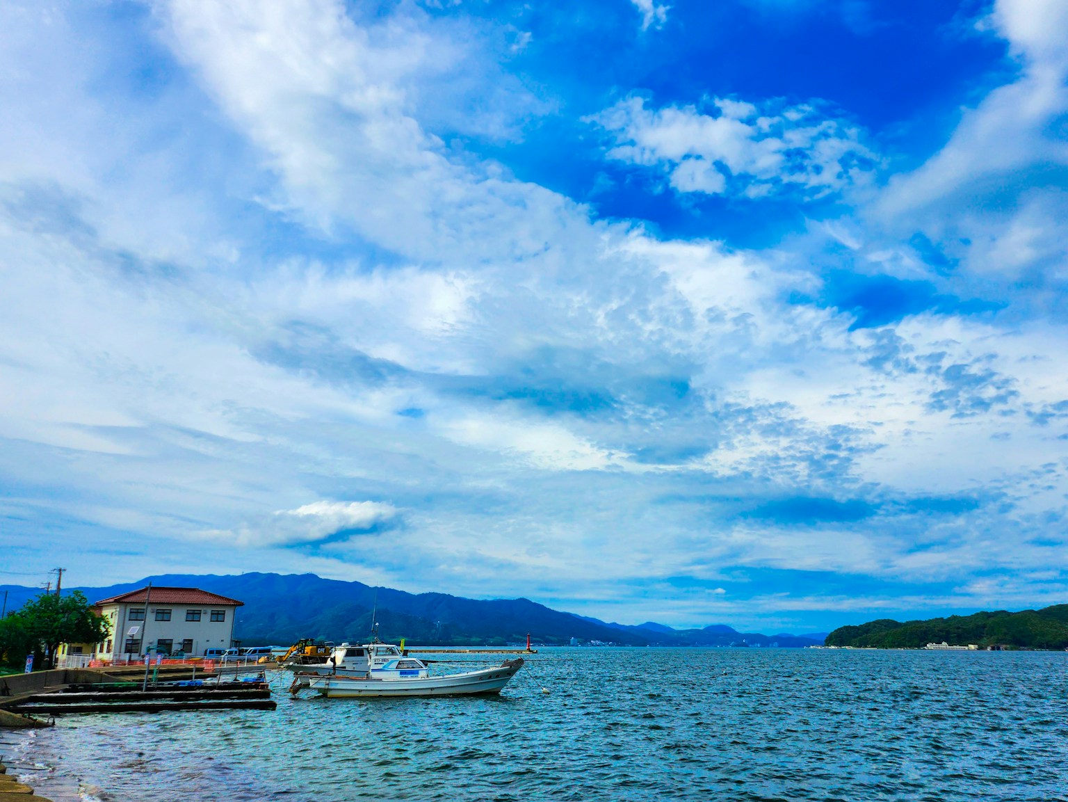 青い空と白い雲が広がる海岸の風景 船と山々が見える