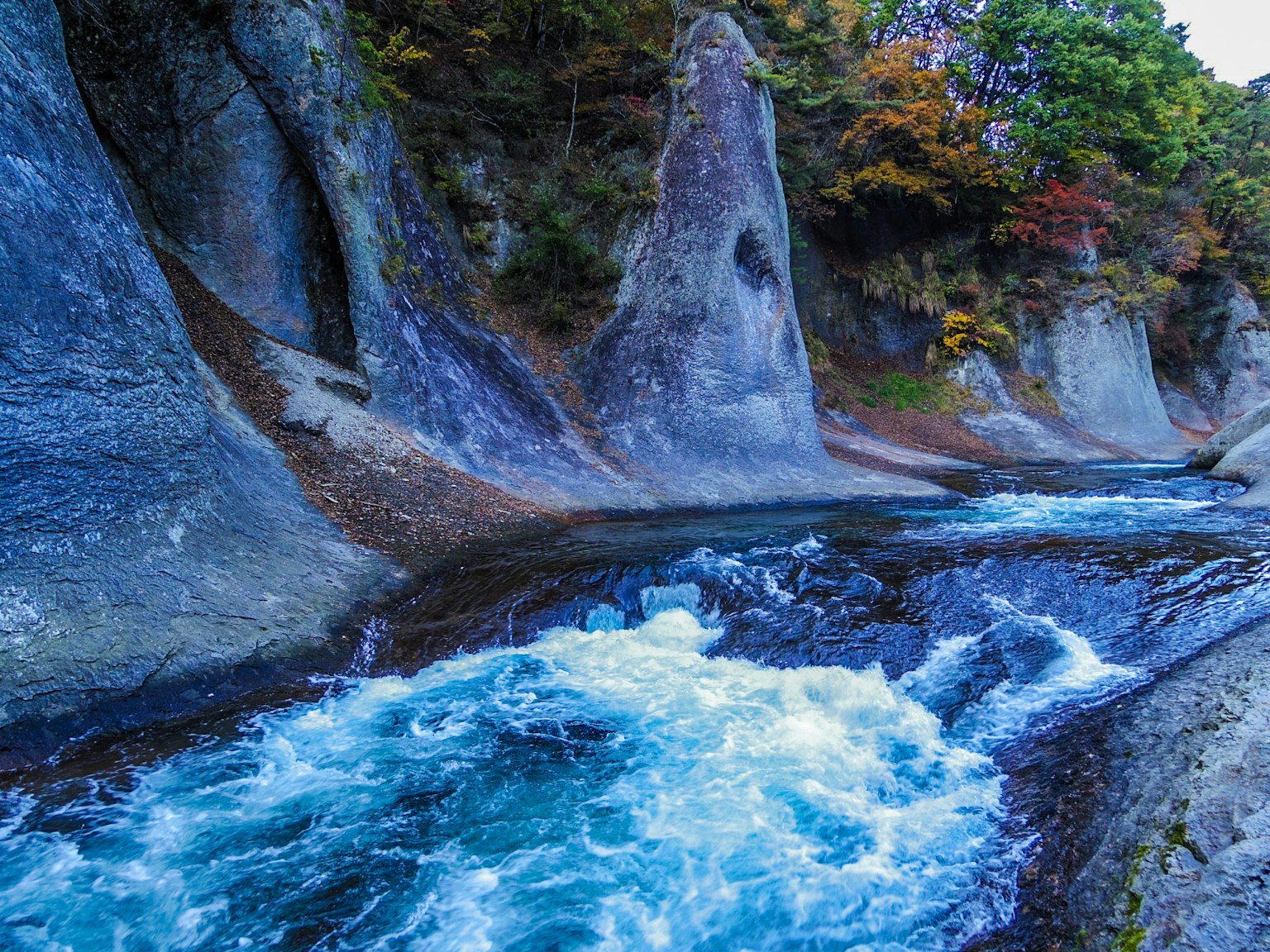 Rivière bleue coulant à travers un paysage rocheux avec feuillage d'automne