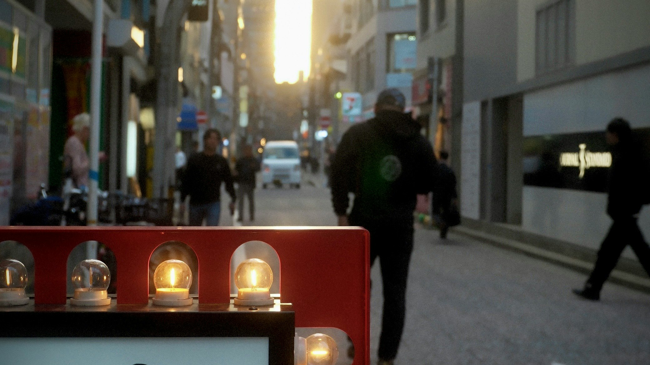 街路に並ぶ赤いガラスドームの装飾と夕暮れの人影