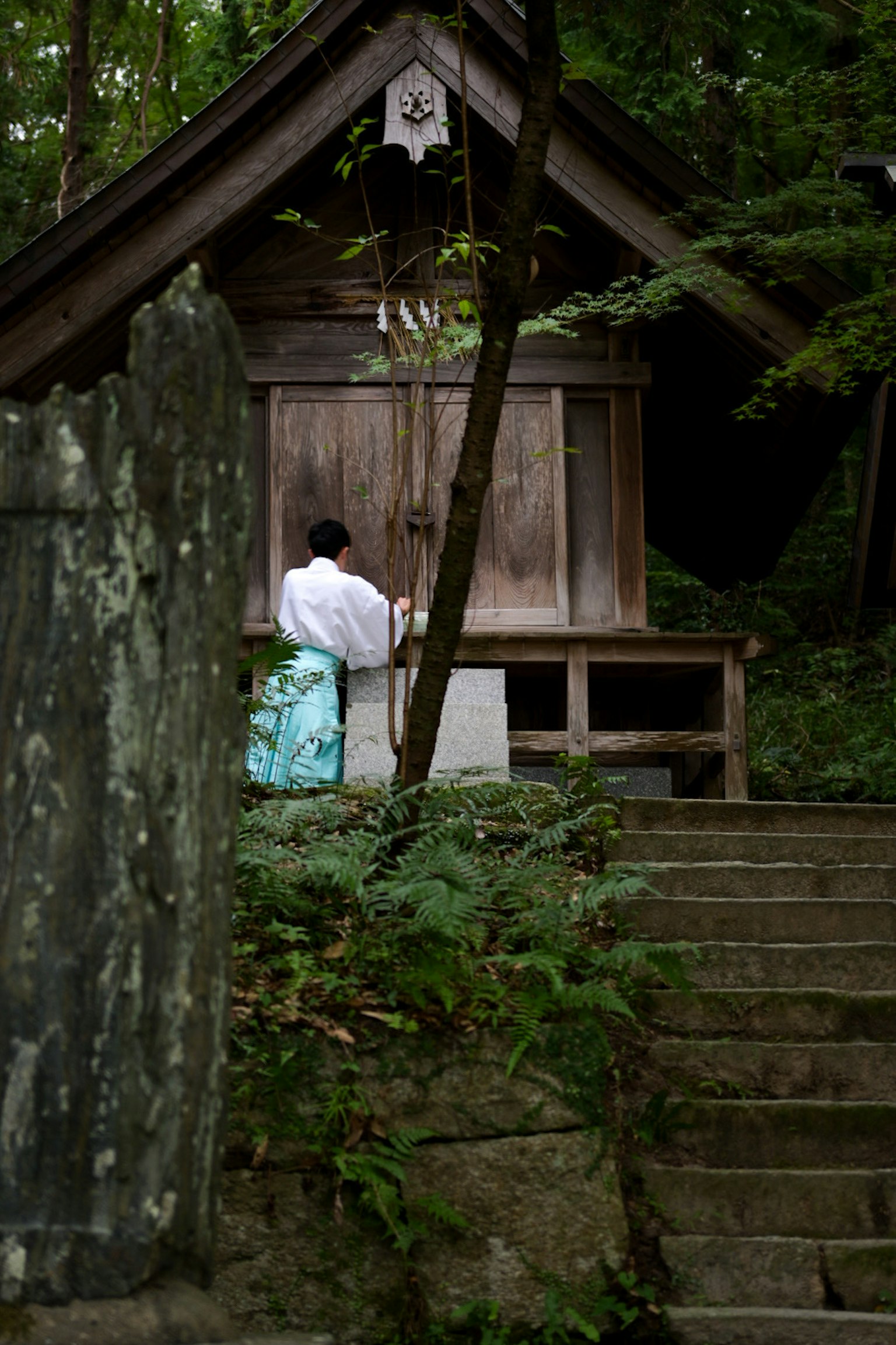 Một người trong trang phục trắng đang mở cửa tại một ngôi đền được bao quanh bởi cây cối