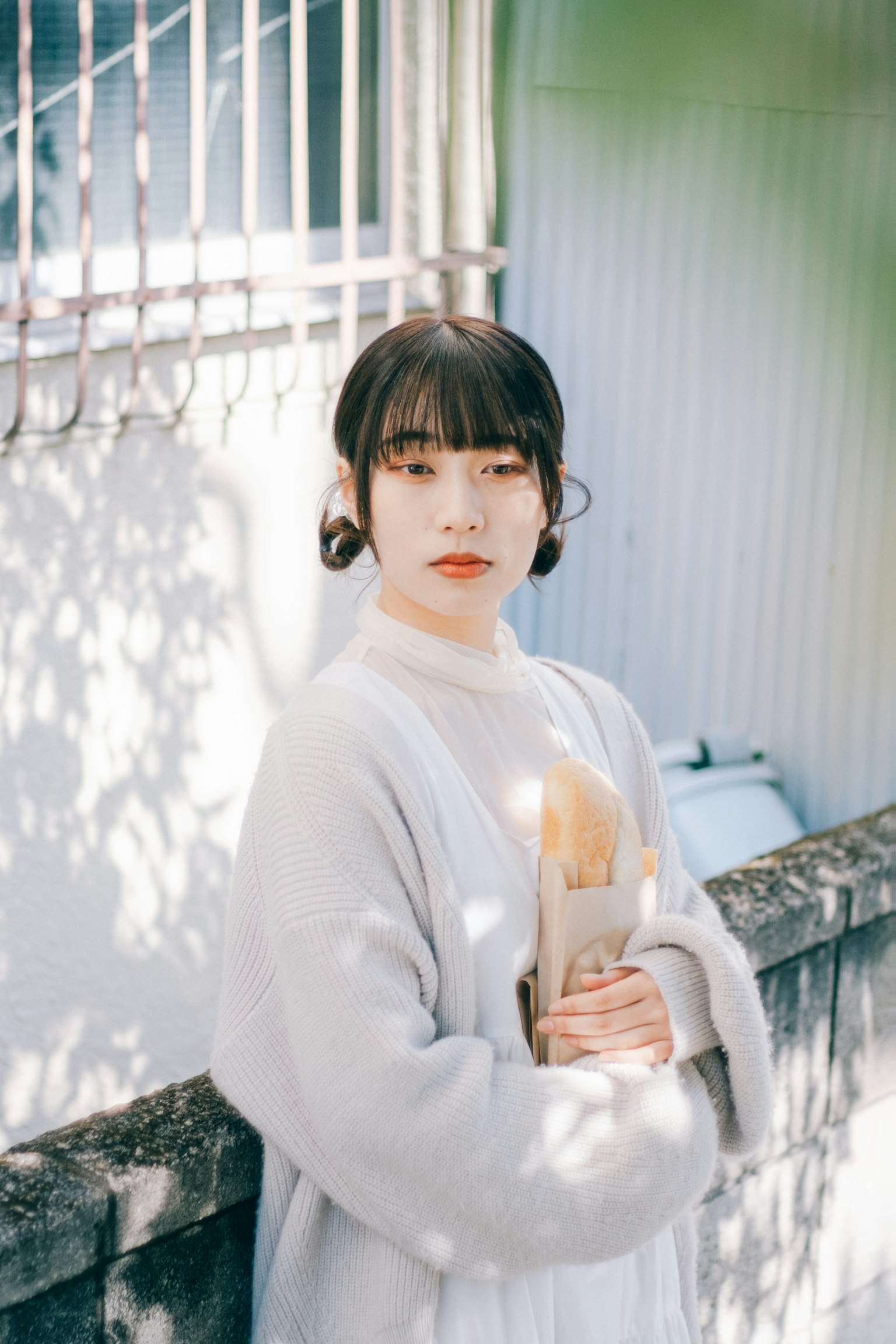 회색 스웨터를 입은 여성이 부드러운 표정을 지으며 꽃다발을 들고 있는 사진으로 배경에는 점이 찍힌 햇빛이 그림자를 만들고 있다