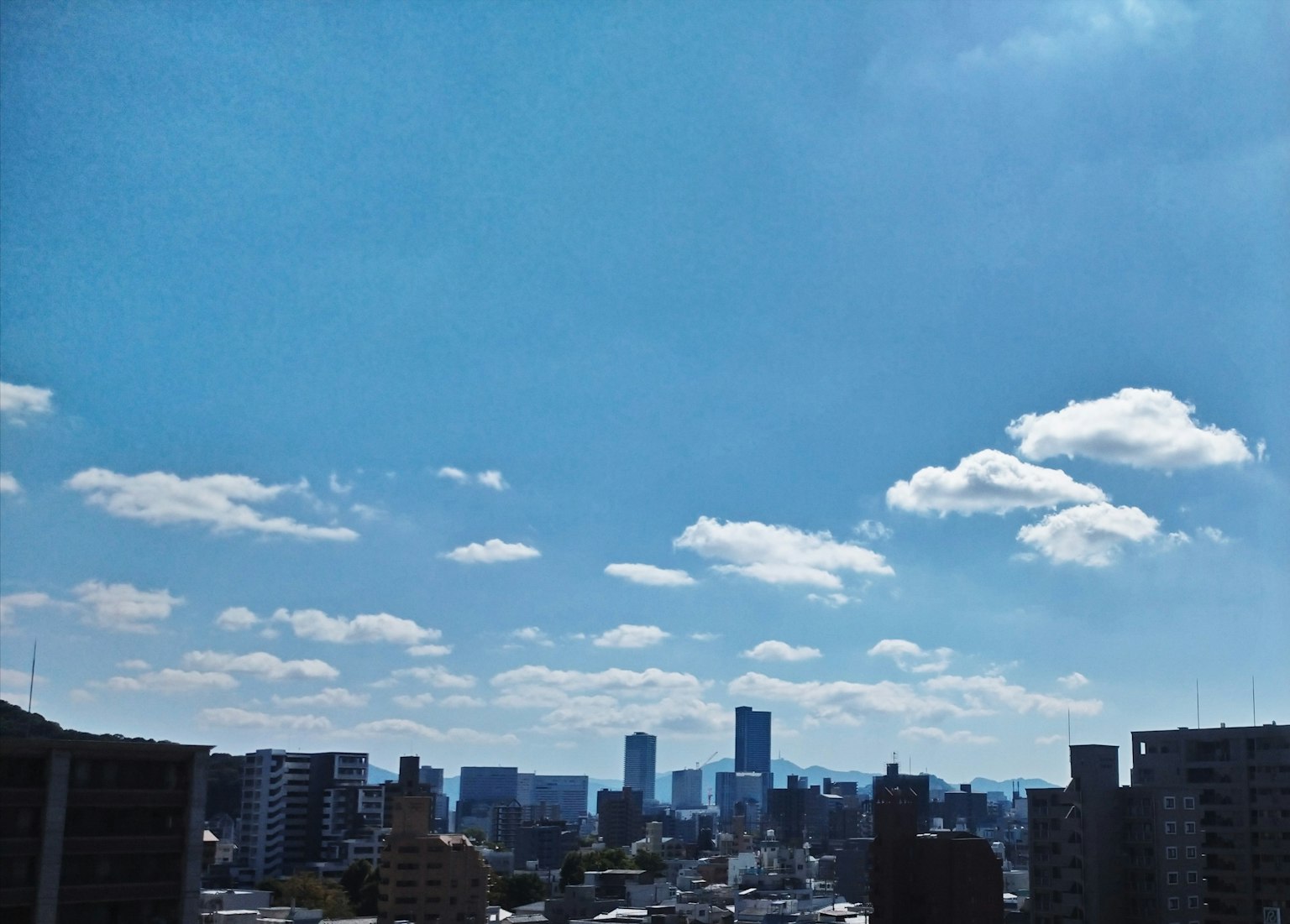 City skyline under a bright blue sky with fluffy white clouds