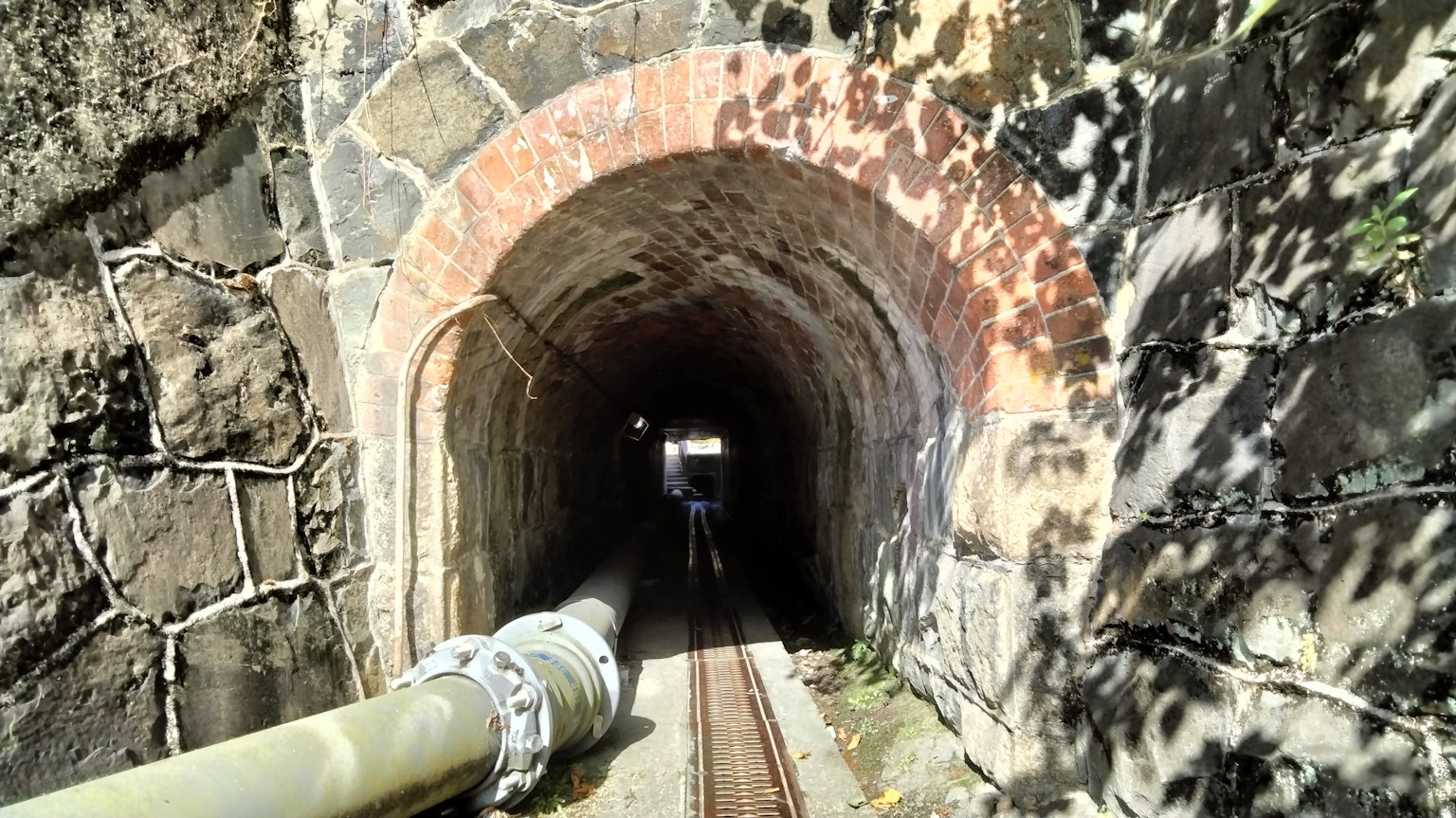 Image d'une entrée de tunnel avec des murs en pierre et des voies ferrées visibles