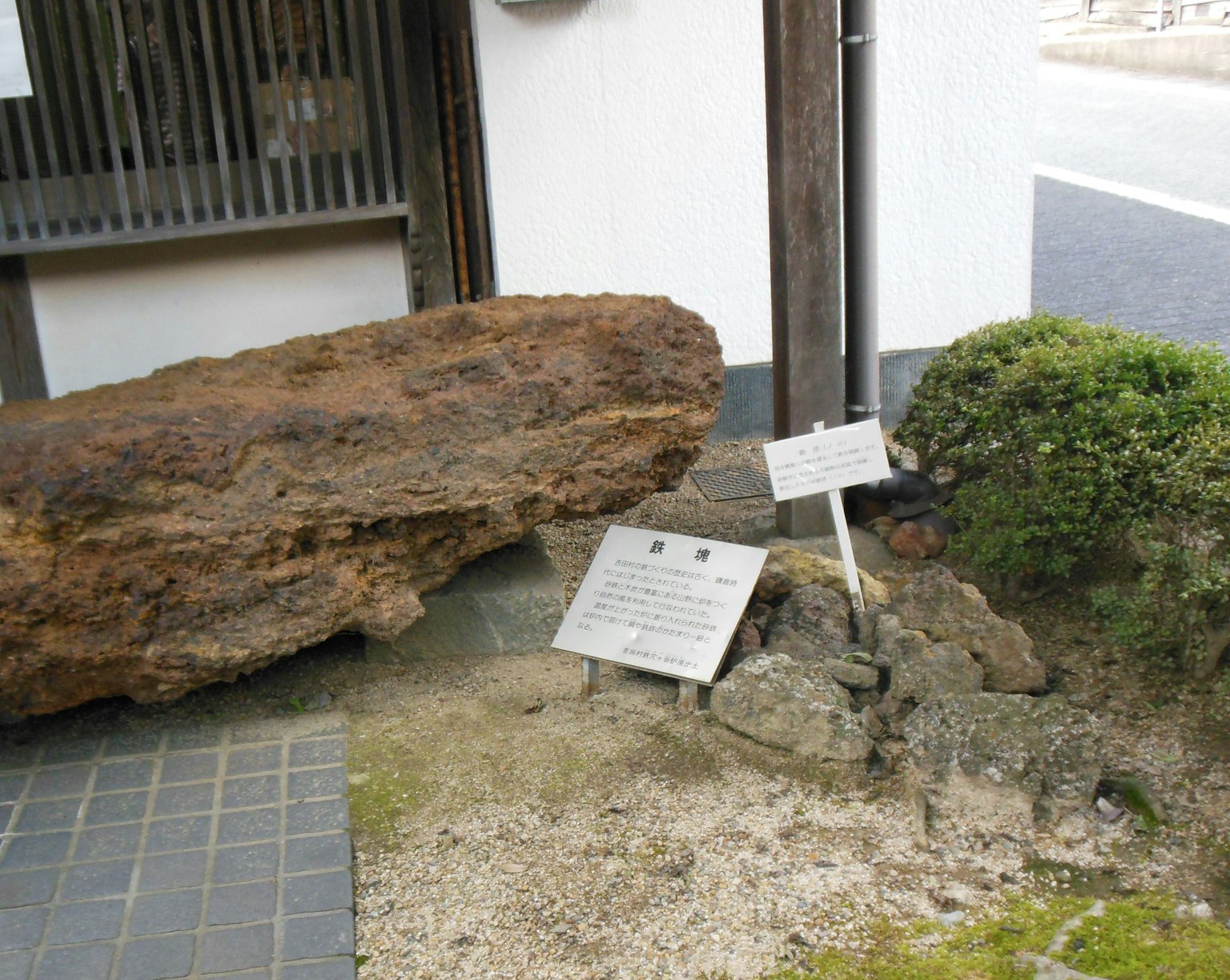 Sebuah patung batu besar dengan papan informasi di depan bangunan tradisional Jepang