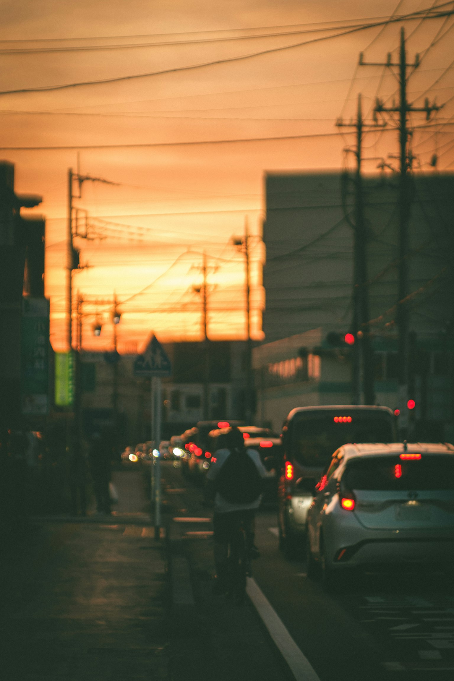 夕焼けの中を走る車と人々のシルエットが見える街の風景