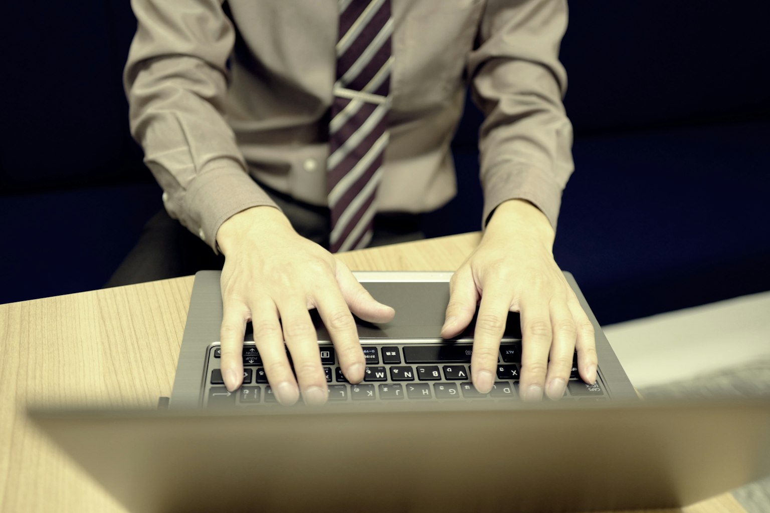 Hände tippen auf einem Laptop in Business-Casual-Bekleidung