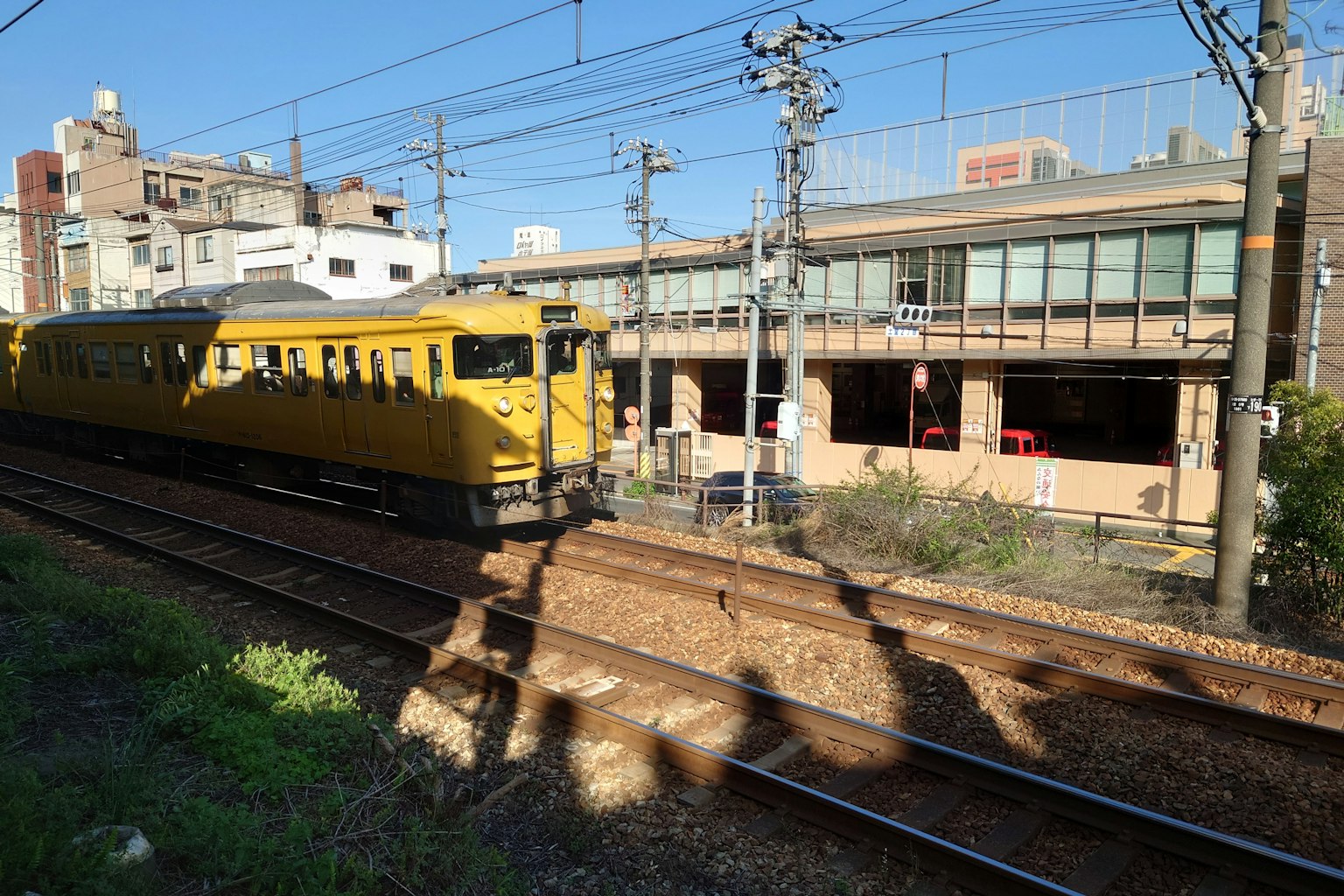 A yellow train passing near a station with buildings in the background