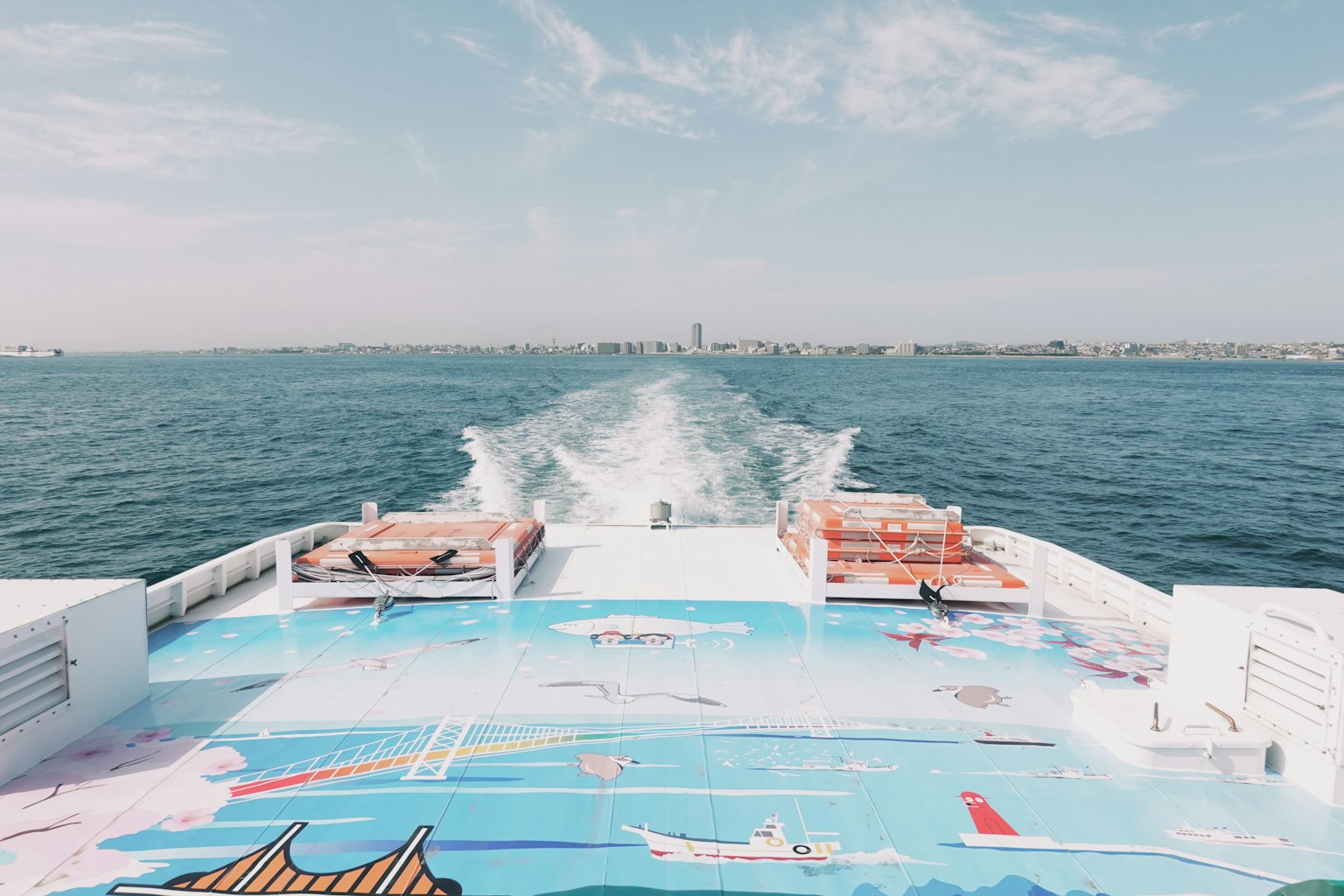 Blick von hinten auf ein Boot mit buntem Kunstwerk auf dem Deck blauer Himmel und Meer im Hintergrund