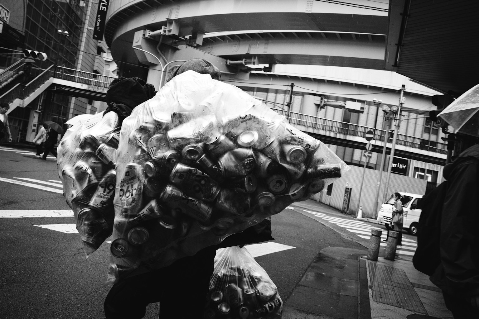 People carrying large bags of trash in a black and white urban setting