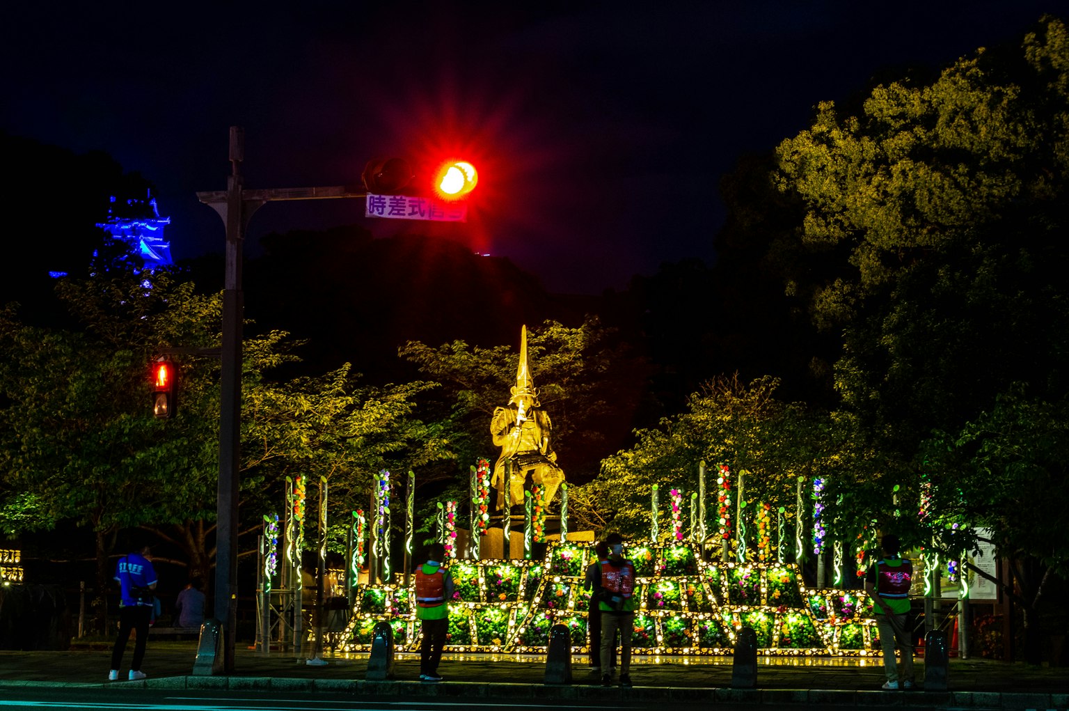 ภาพตอนกลางคืนของรูปปั้นที่ล้อมรอบด้วยการตกแต่งหลากสีในสวน