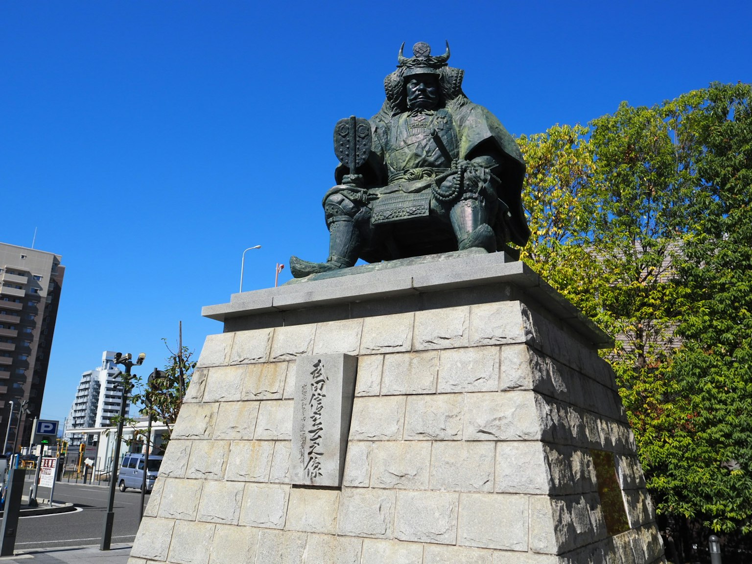 Una estatua de un samurái sentada sobre un pedestal de piedra bajo un cielo azul