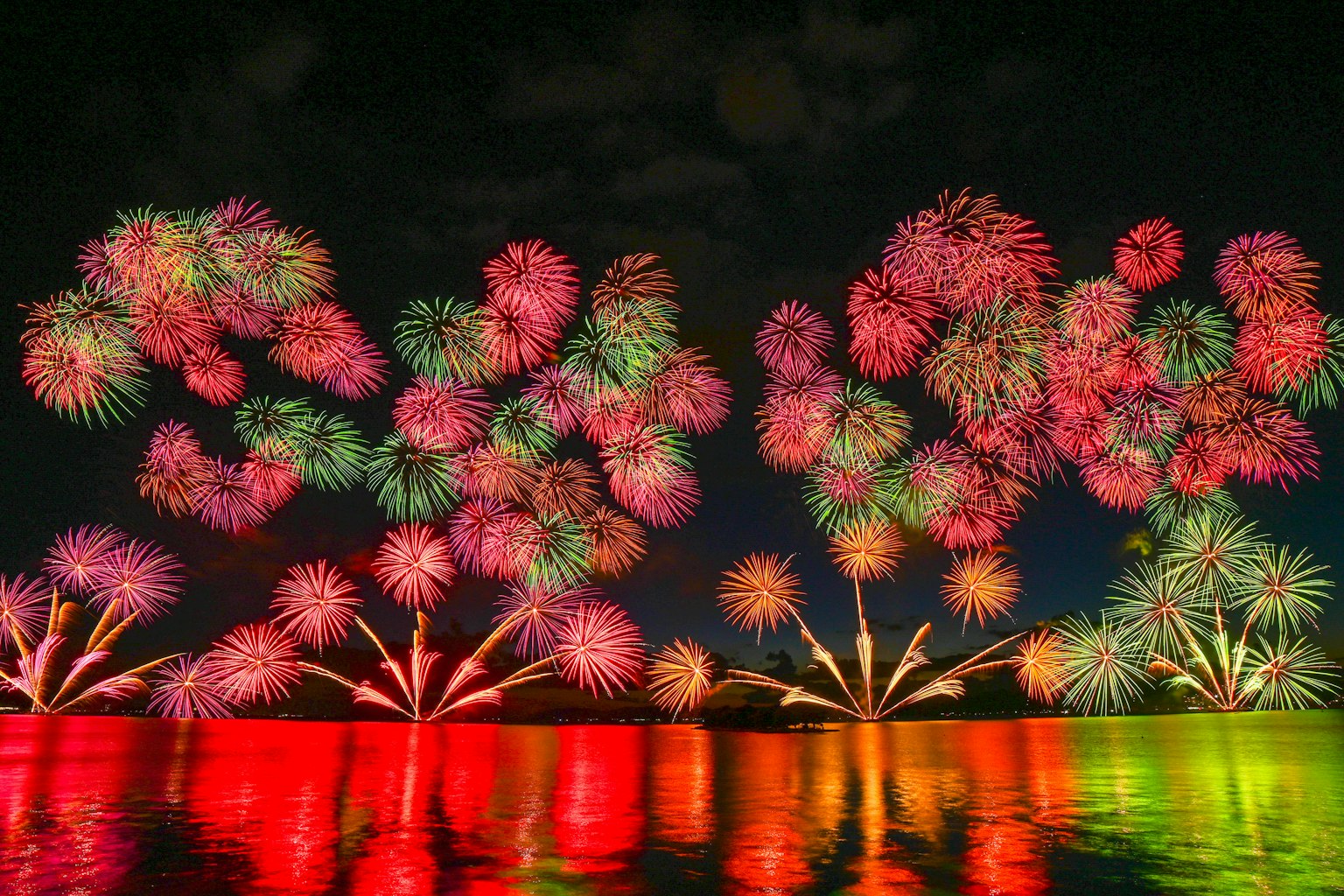 夜空を彩るカラフルな花火が水面に映る美しい光景