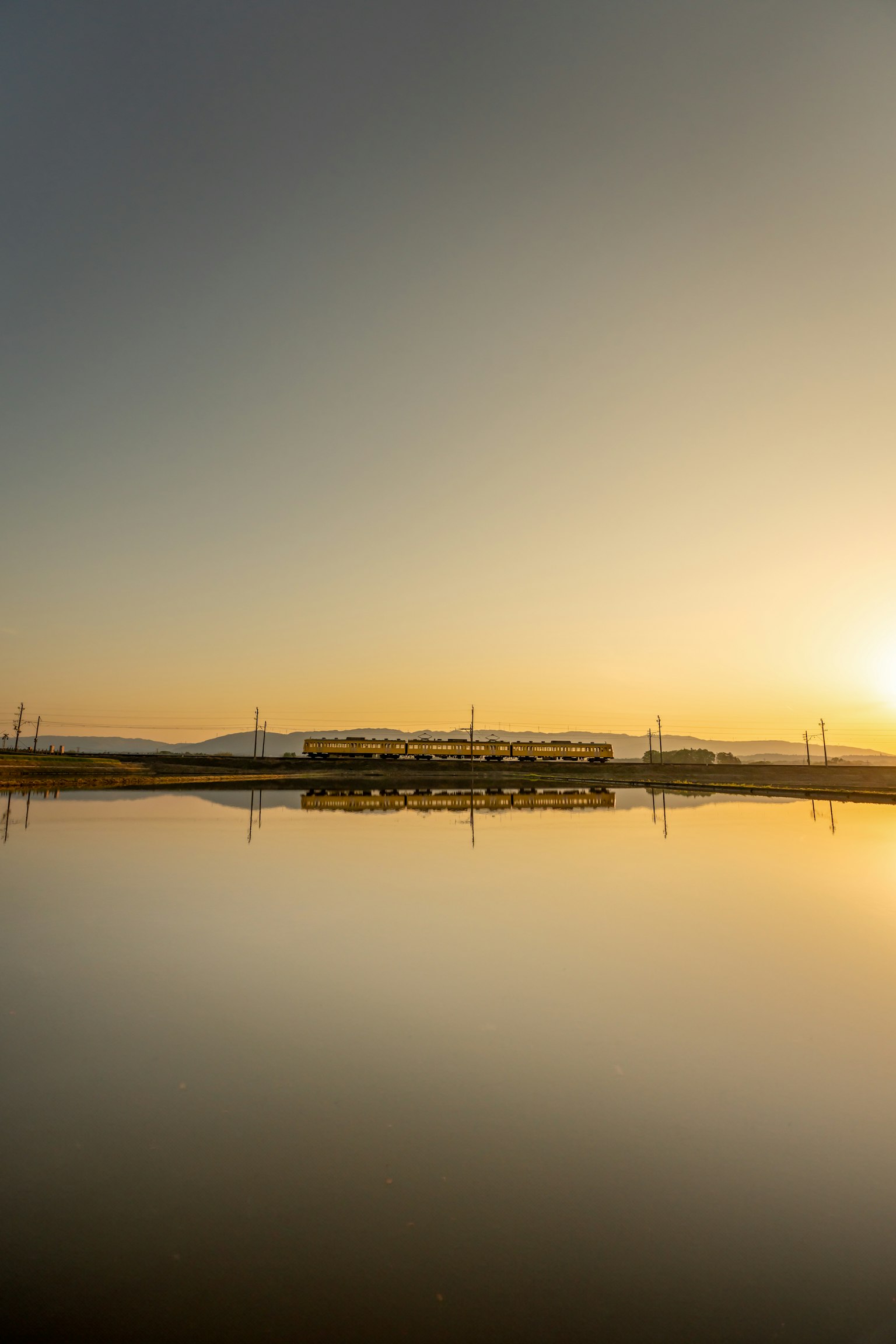 Ruhiger See, der den Sonnenuntergang und Silhouetten von Stromleitungen spiegelt