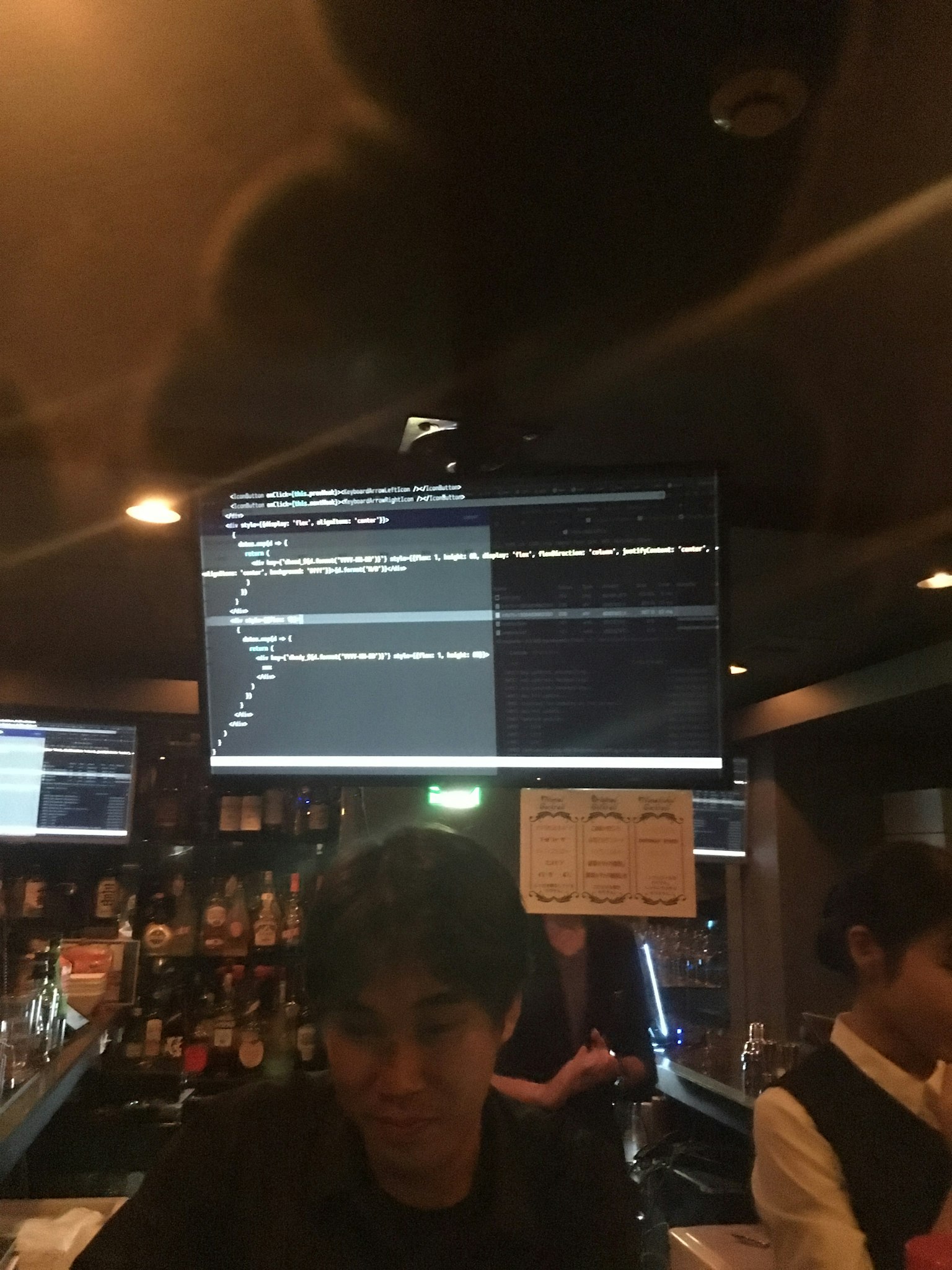 Junger Mann, der an einer Bar arbeitet, mit einem Monitor im Hintergrund, der Programmiercode anzeigt