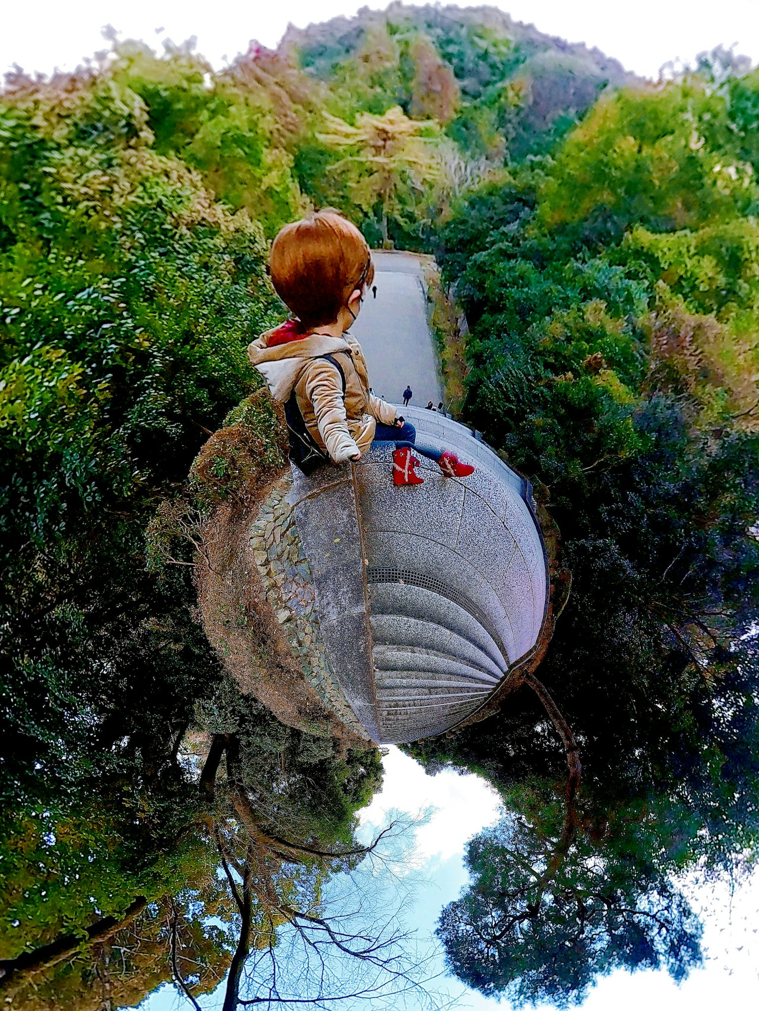 Un niño sentado en una esfera de piedra surrealista rodeado de vegetación exuberante