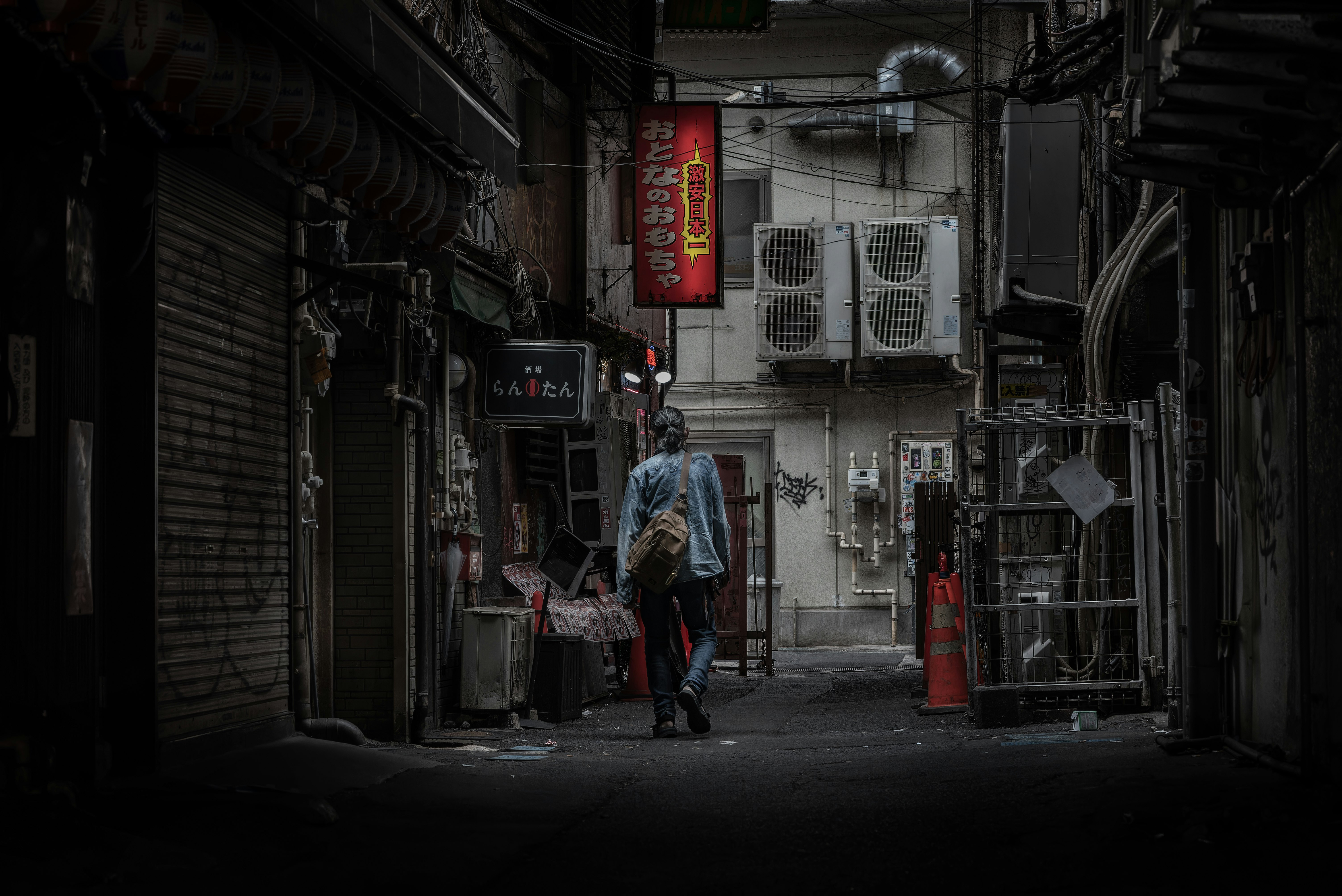 路地の奥に立つ人物と看板のある狭い商店街の通り