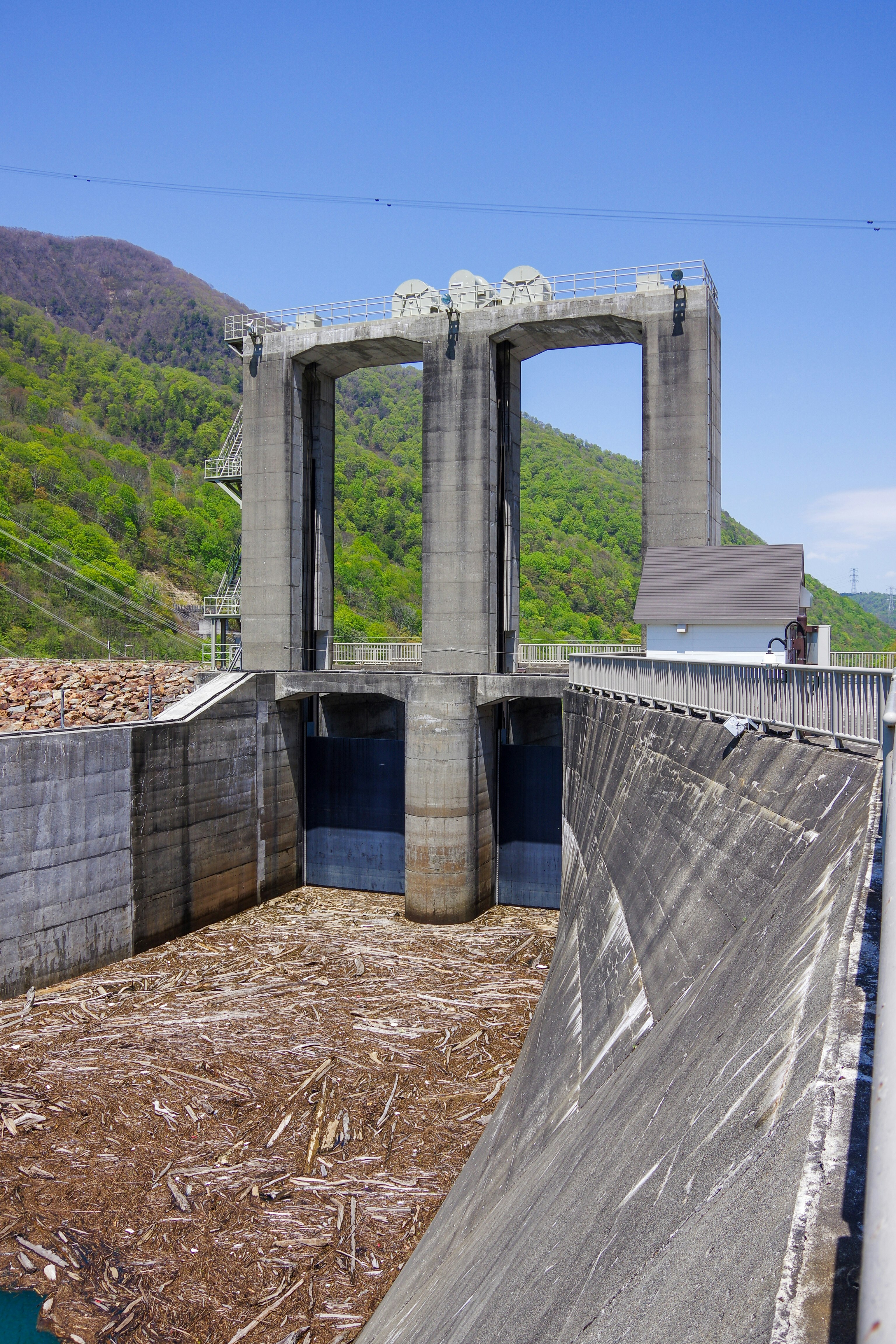 ダムの放水路と巨大なコンクリートアーチ、山の緑を背景にした発電所の設備