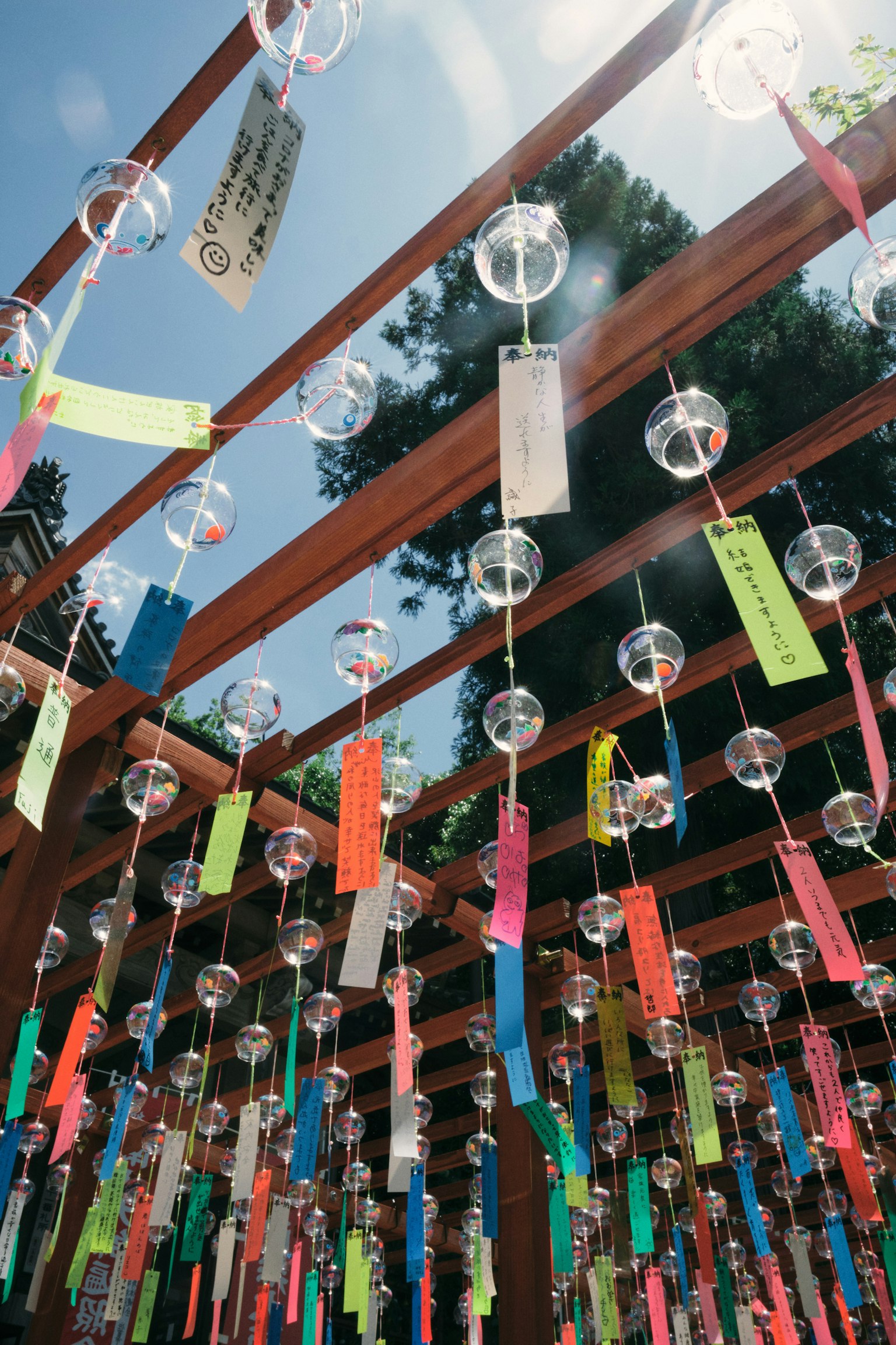 Bunte Windspiele, die von einer Holzpergola hängen, von unten gesehen mit lebhaften Papierstreifen