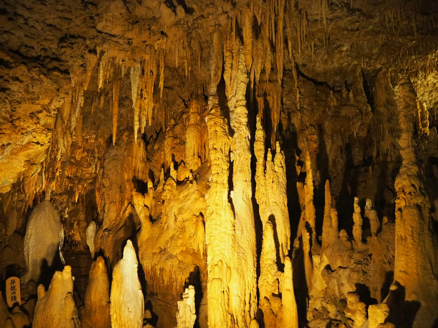 Innenansicht einer Höhle mit von goldenem Licht beleuchteten Stalaktiten und Stalagmiten
