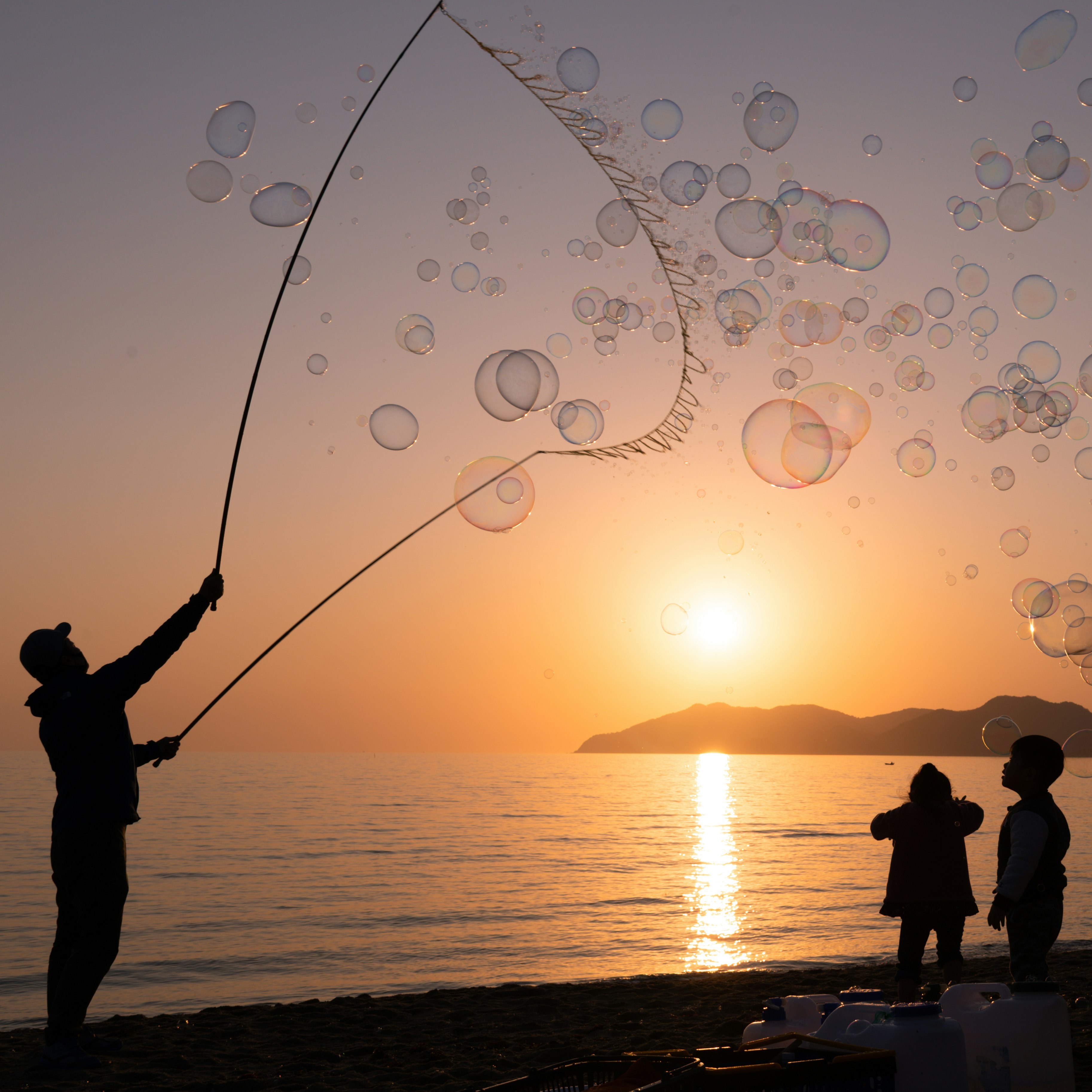 夕日に照らされた海辺で釣りをする人々のシルエット