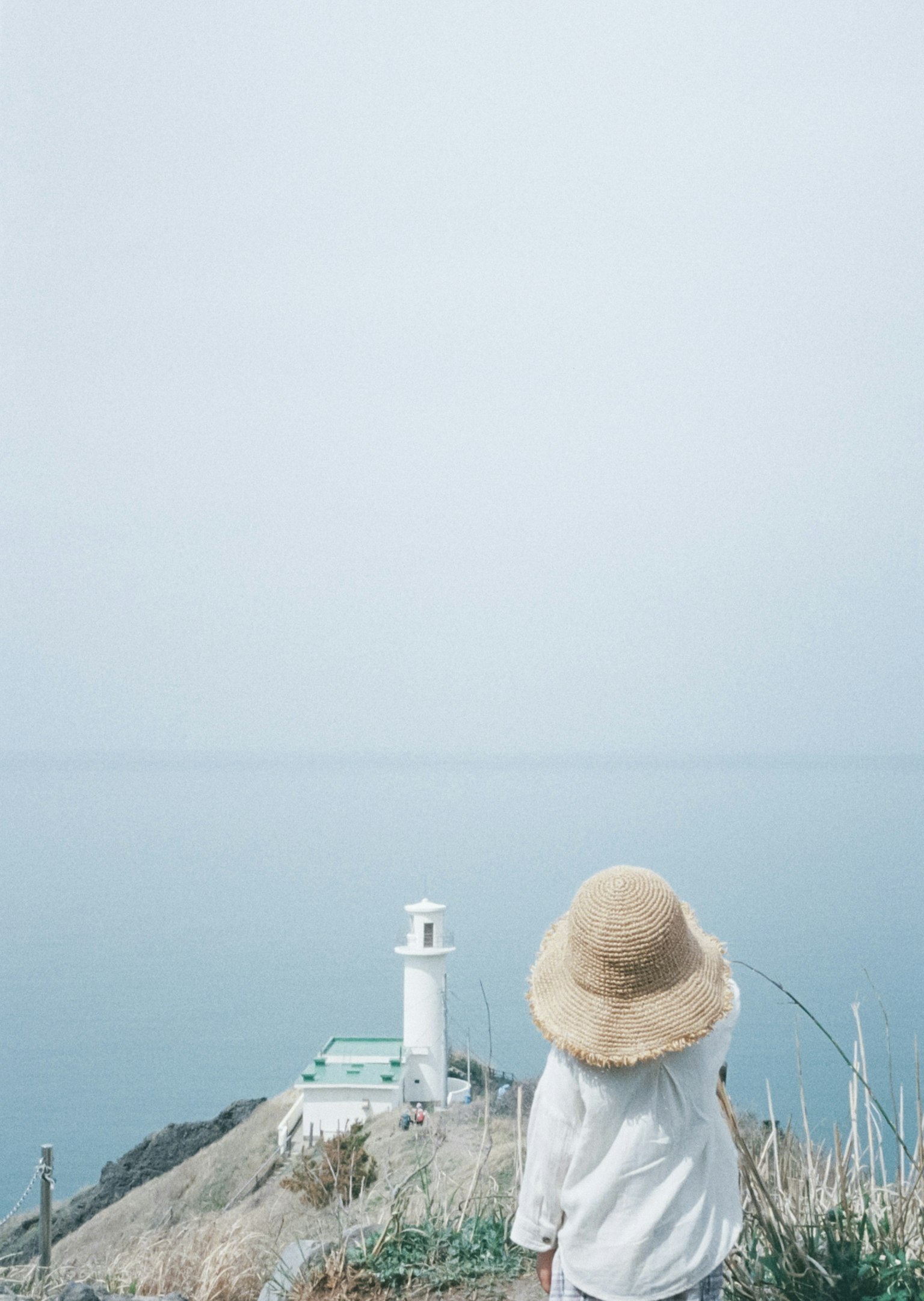 Child wearing a hat gazing at the sea and lighthouse