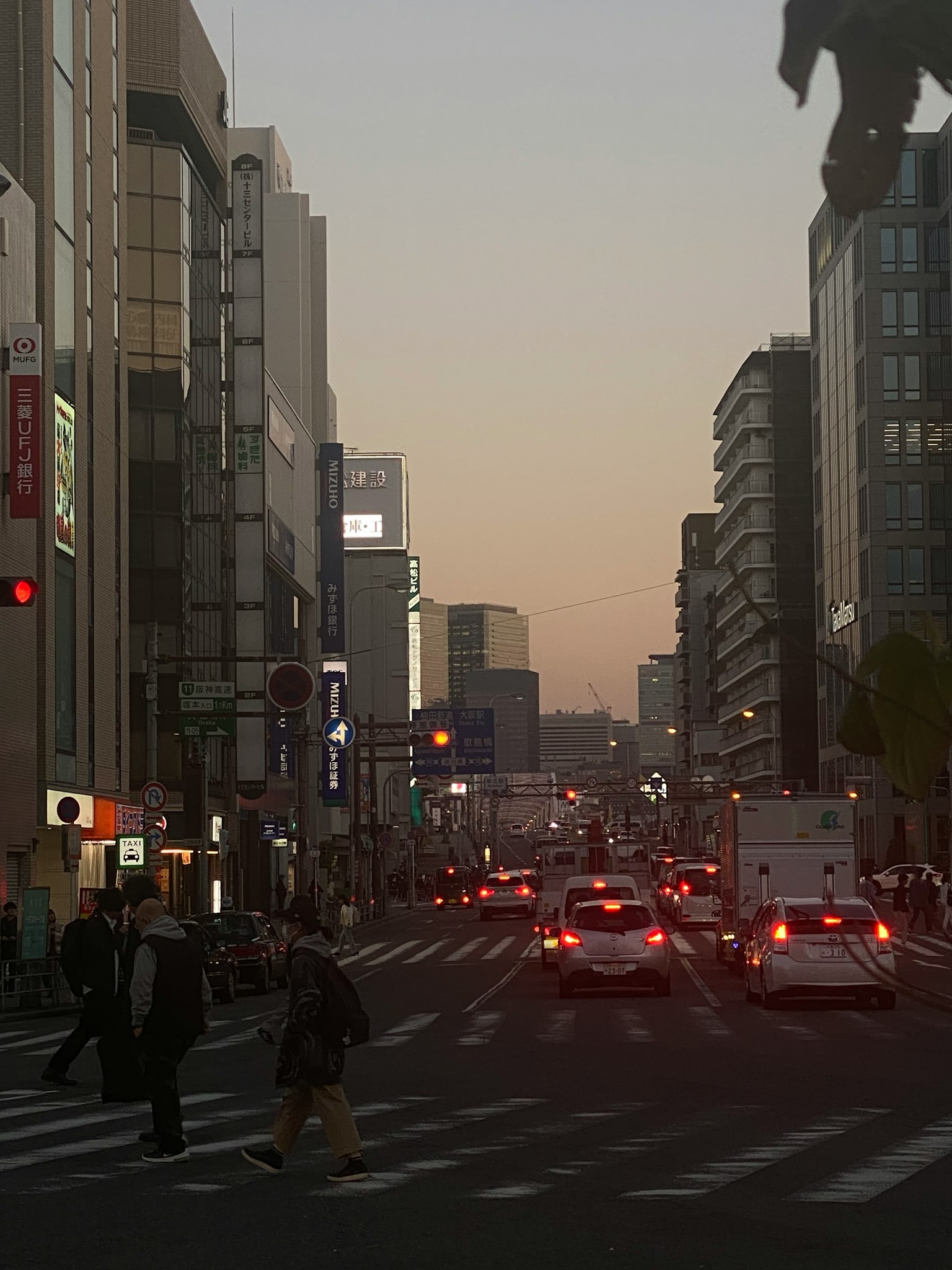 Cityscape at dusk with cars and pedestrians on the road tall buildings in the background