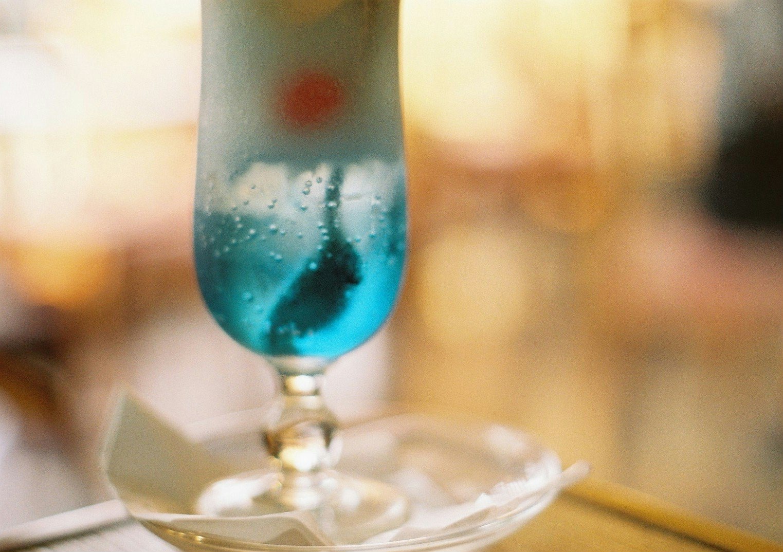 blue cocktail glass with bubbly drink and tableware on a dining table