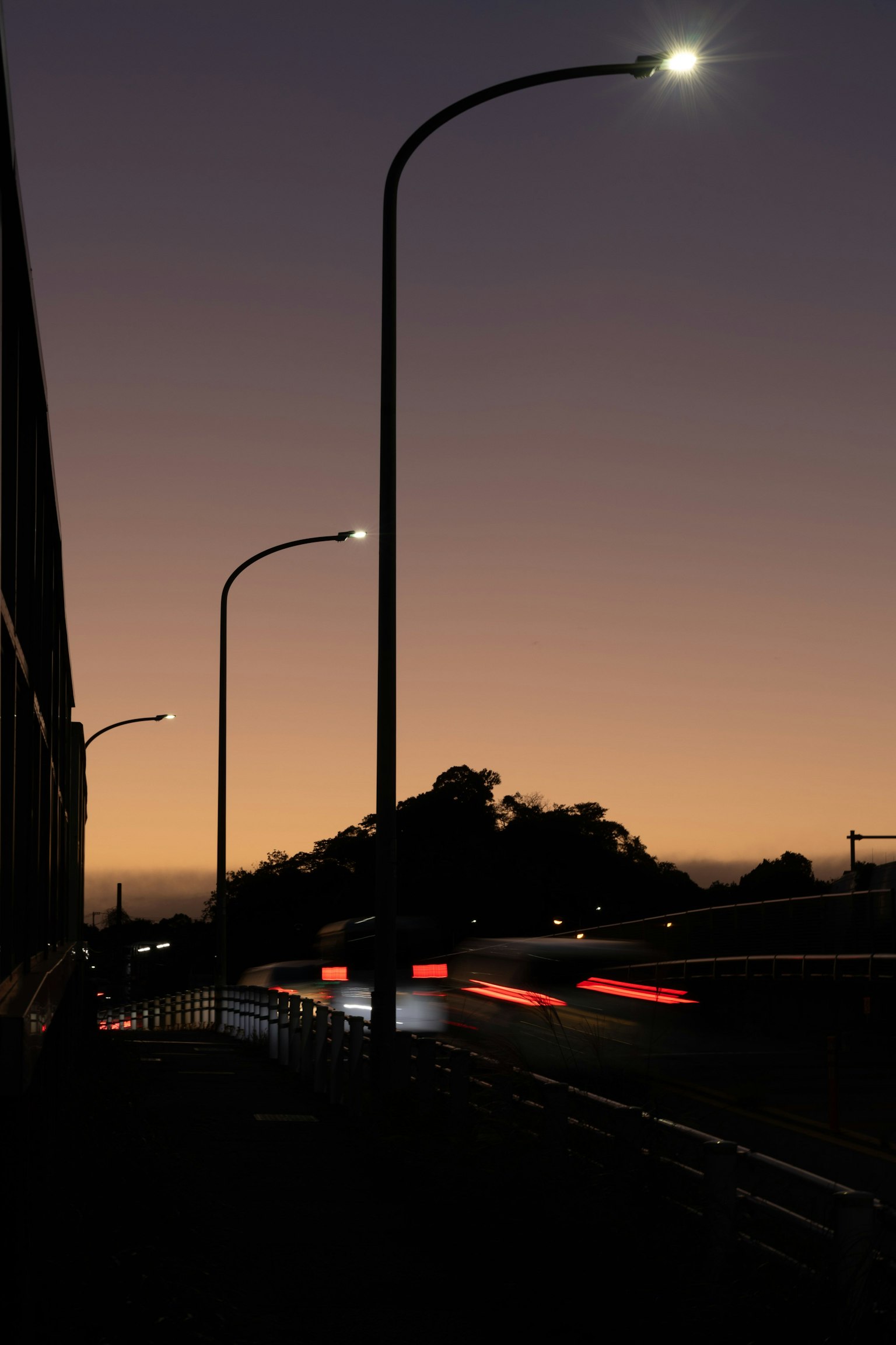 Bóng đèn đường silhouetted trước bầu trời hoàng hôn với đèn xe di chuyển