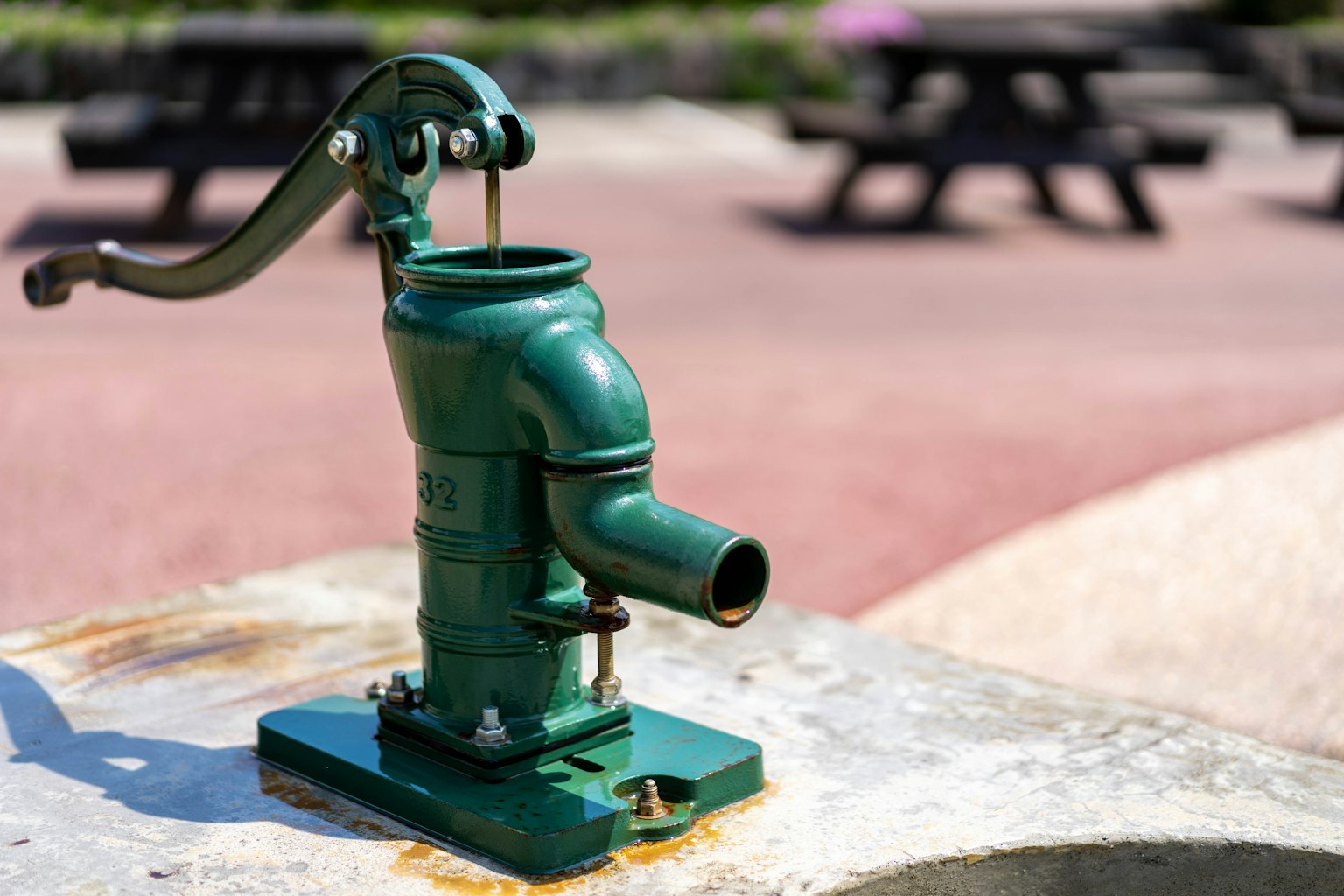 Una pompa a mano verde situata vicino a panchine da picnic in un parco